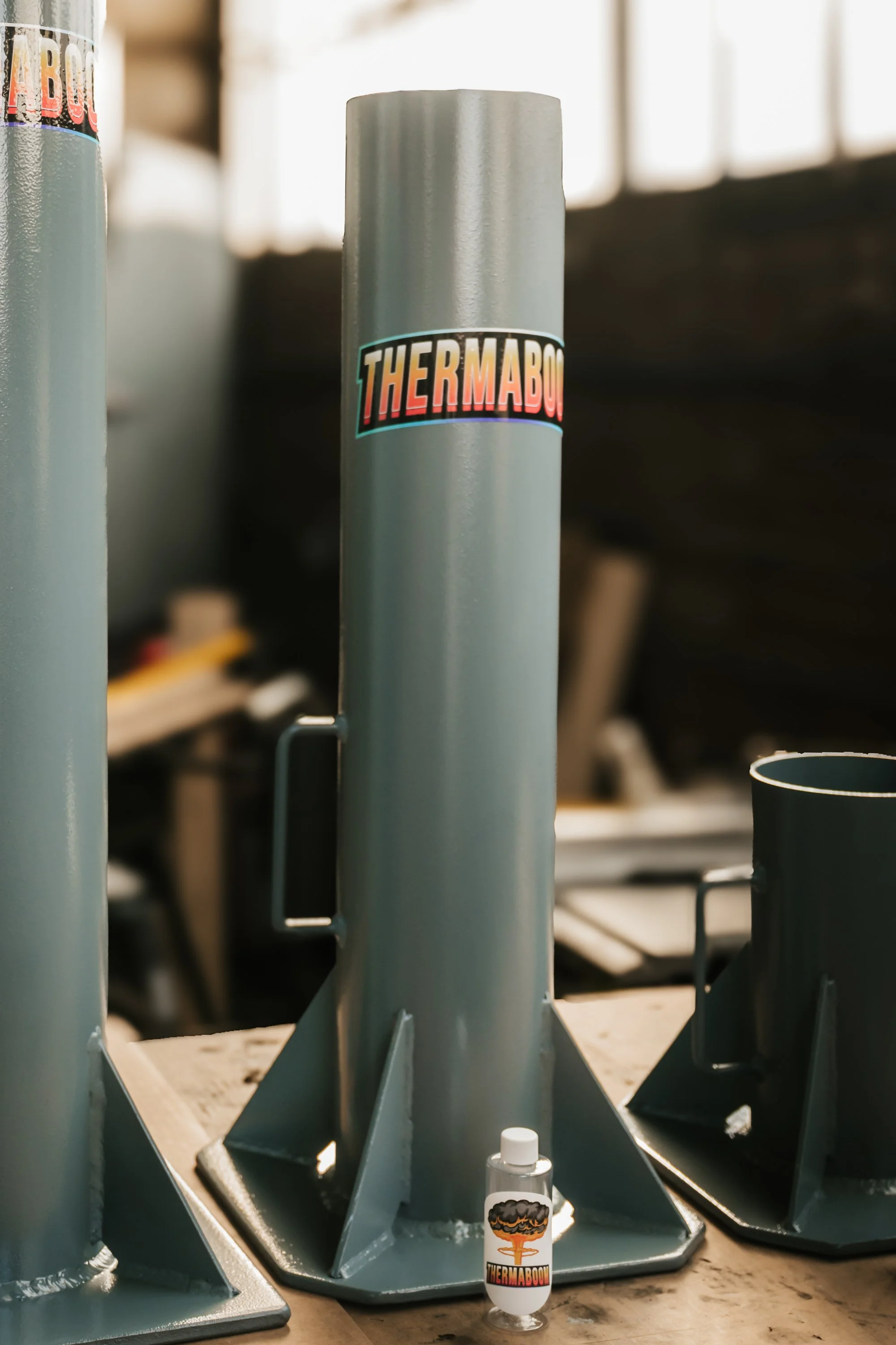 A metal rocket with a label reading "THERMABOOM" standing on a wooden surface.