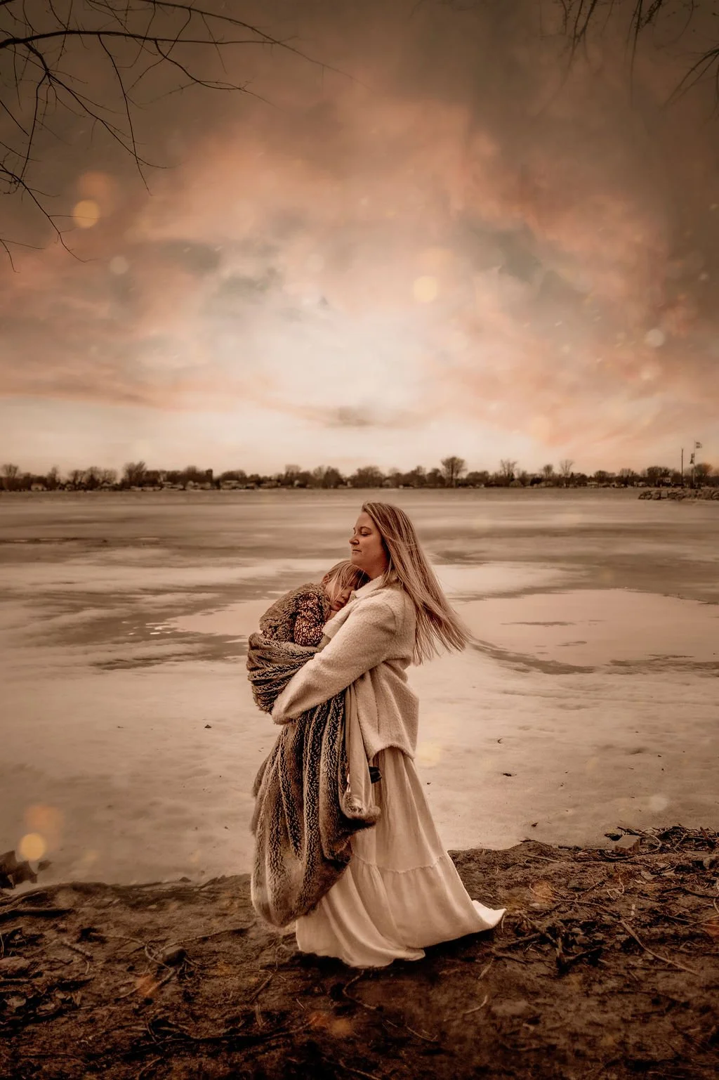 Une femme enveloppe un enfant dans ses bras près d'un lac gelé avec un ciel aux couleurs chaudes au crépuscule.