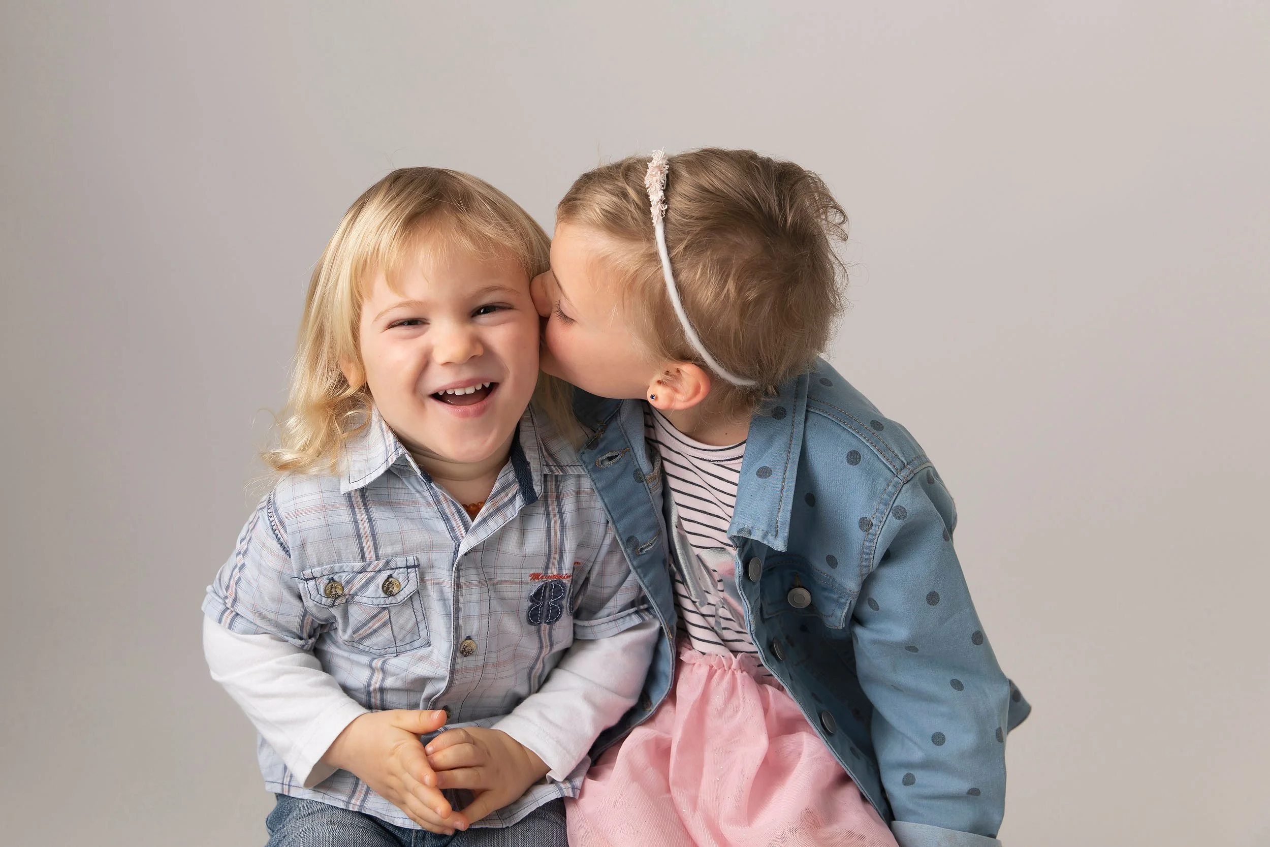 Two young children, a boy and a girl, sharing a happy moment; the girl is kissing the boy on the cheek, and the boy is smiling.