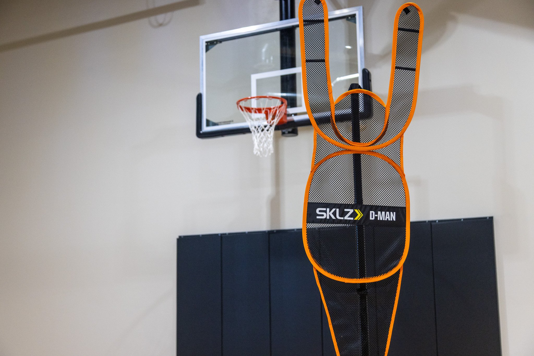 Indoor basketball court with a basketball hoop, and a Slaz D-Man basketball shooting obstacle system in the foreground.