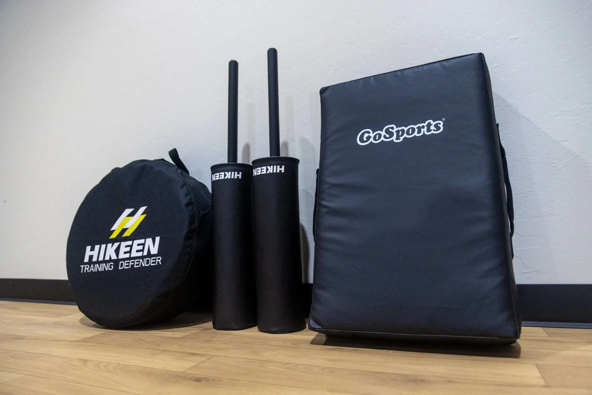 Home workout equipment including a black Hikeen Training Defender bag, two black HIKEN foam rollers, a black GoSports padded mat, and a black HIKEN cushion.