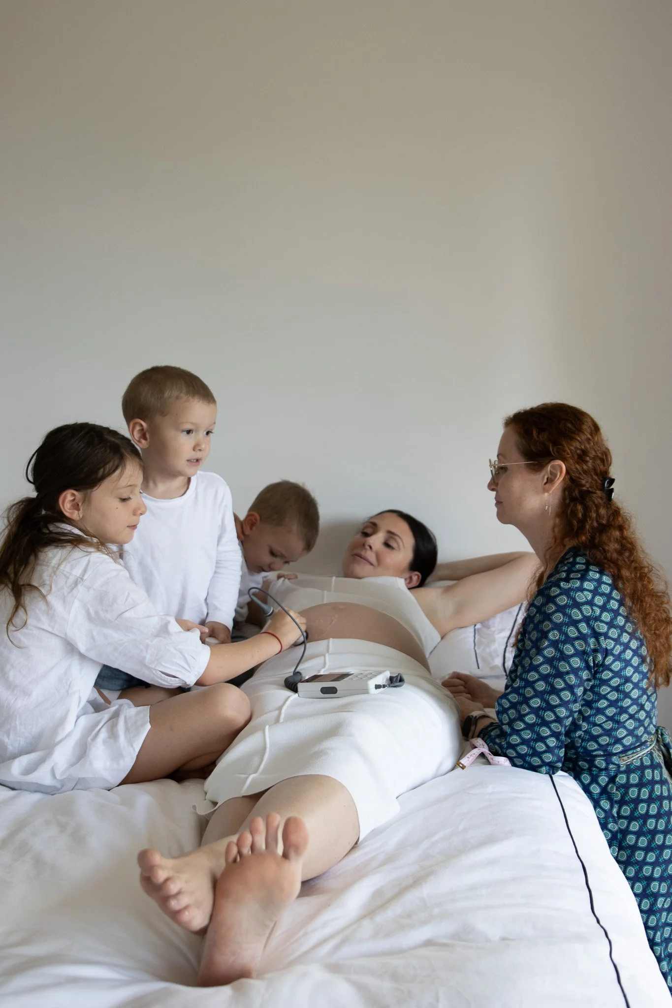 A woman in a hospital bed surrounded by children and a nurse, with medical equipment on her abdomen.
