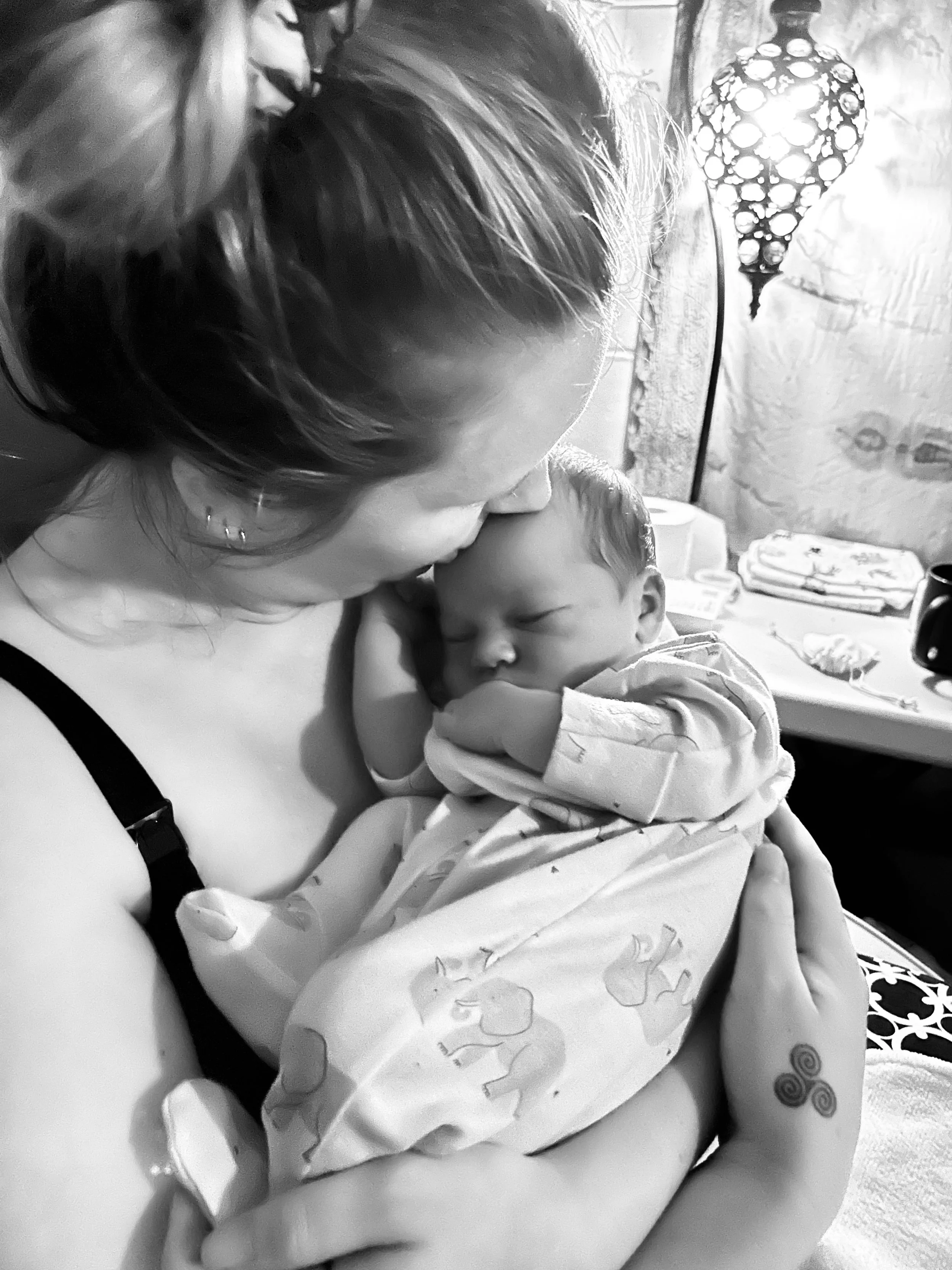 A woman is holding and kissing a sleeping newborn baby wrapped in a blanket with animal prints.