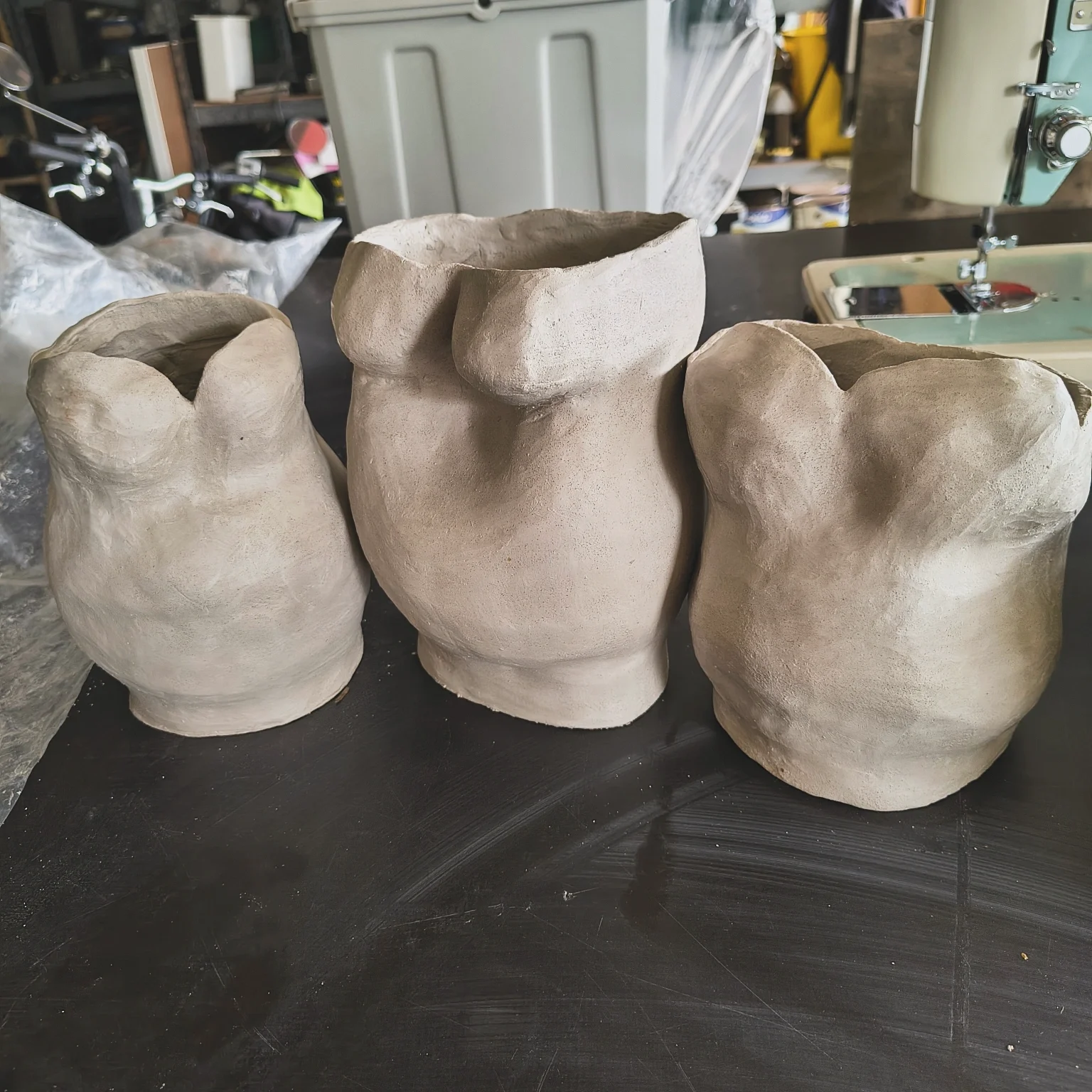 Four unfinished ceramic vases on a dark work surface in a workshop.