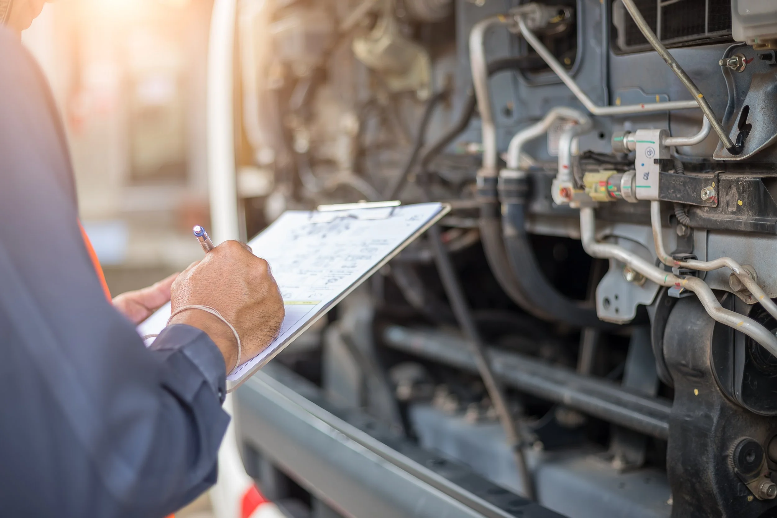 A mechanic inspecting an engine with a clipboard in hand.
