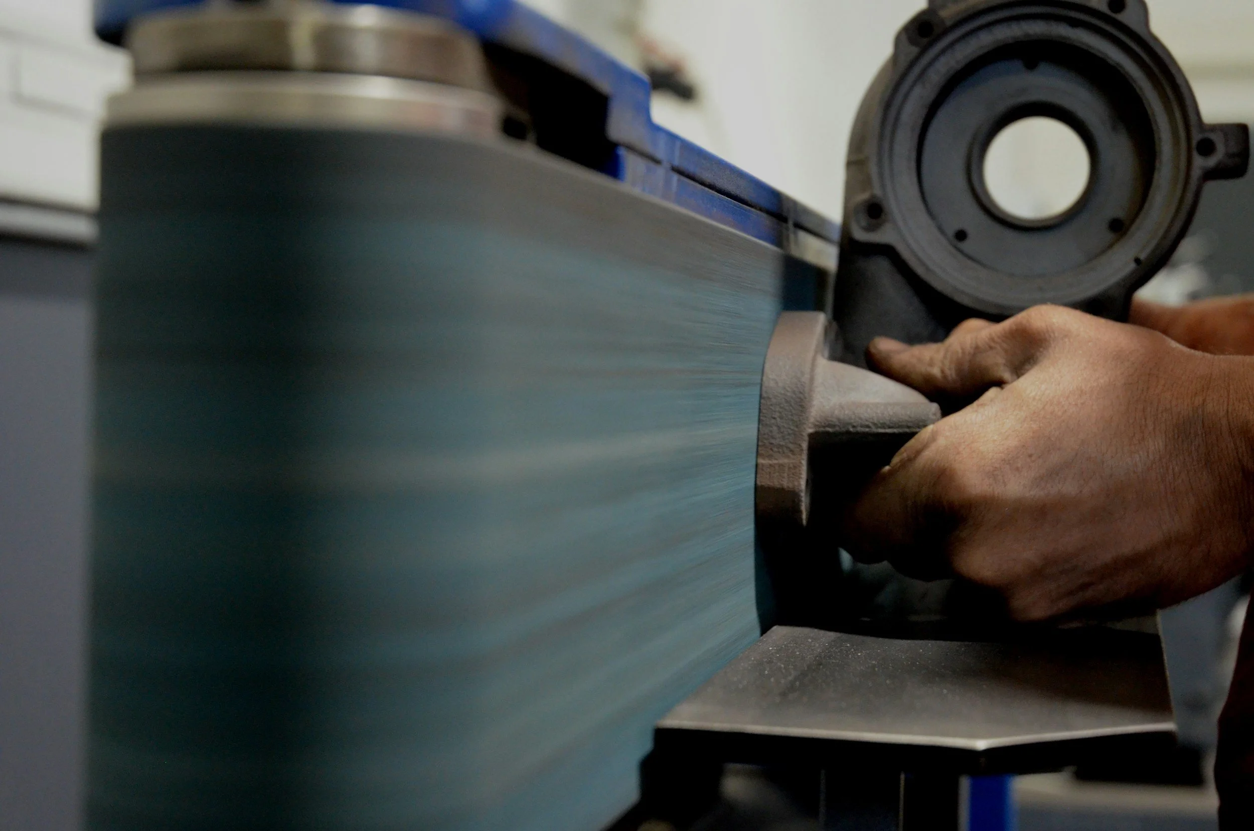 Person using a handheld tool to shape or smooth a piece of blue material on a machine in a workshop.