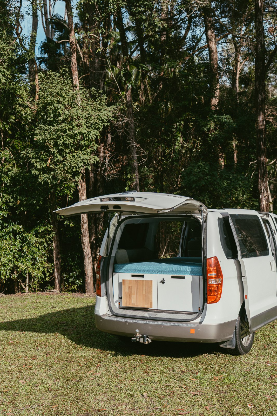 Camper van with open rear hatch in a forested area