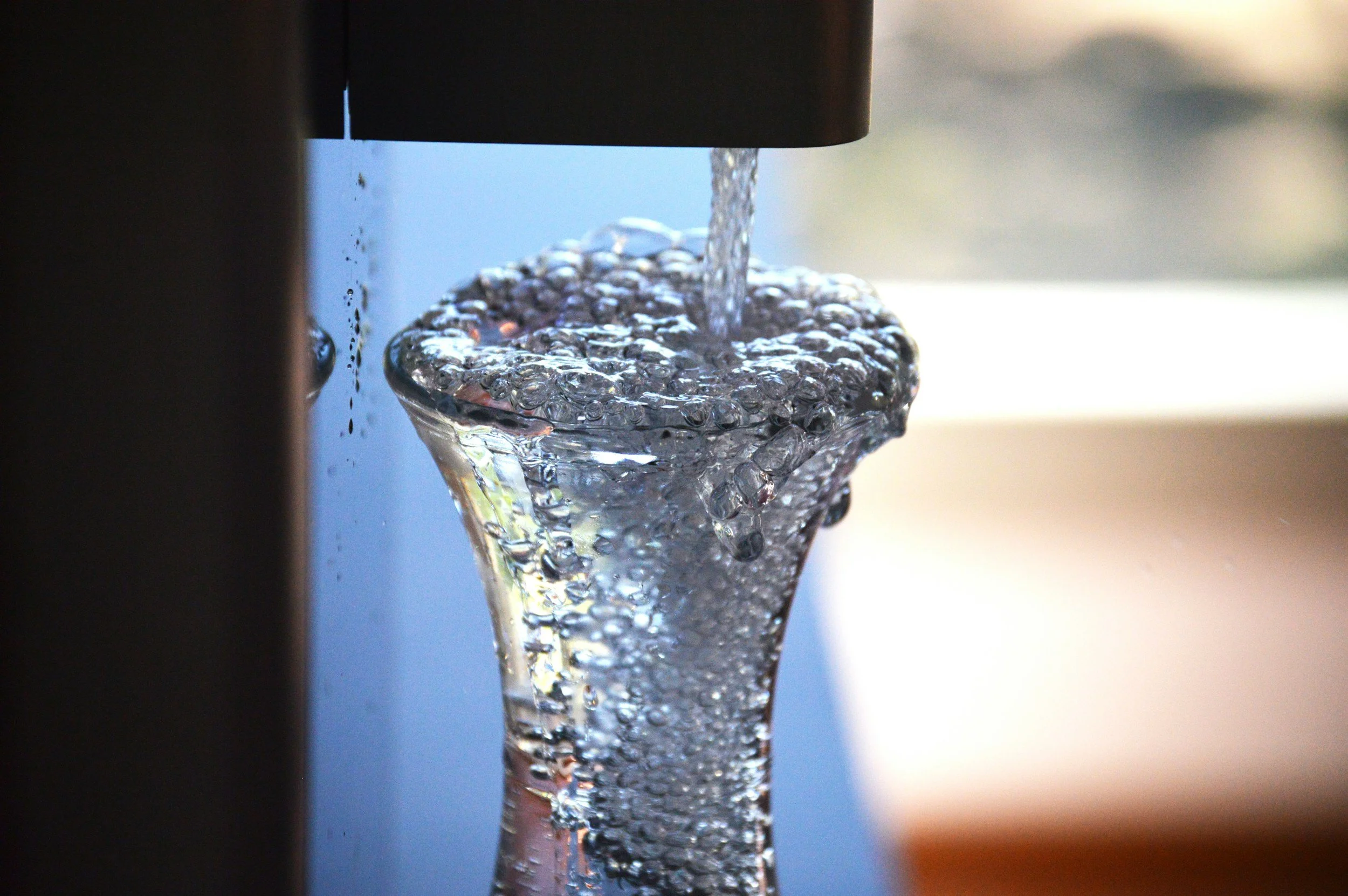 Close-up of water flowing into a glass with bubbles forming at the surface.