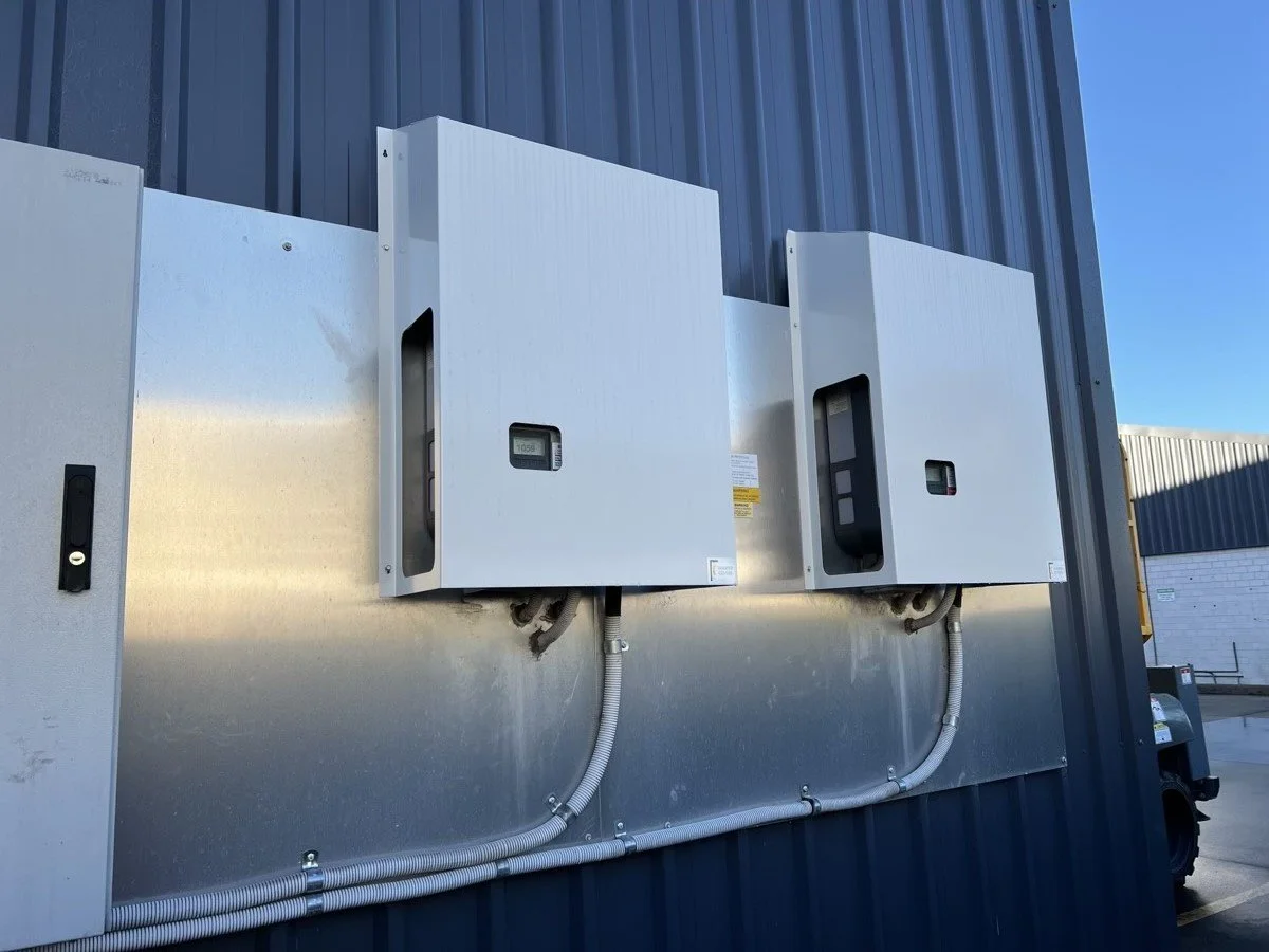 Two white electrical enclosures mounted on an exterior metal wall with conduit connections.