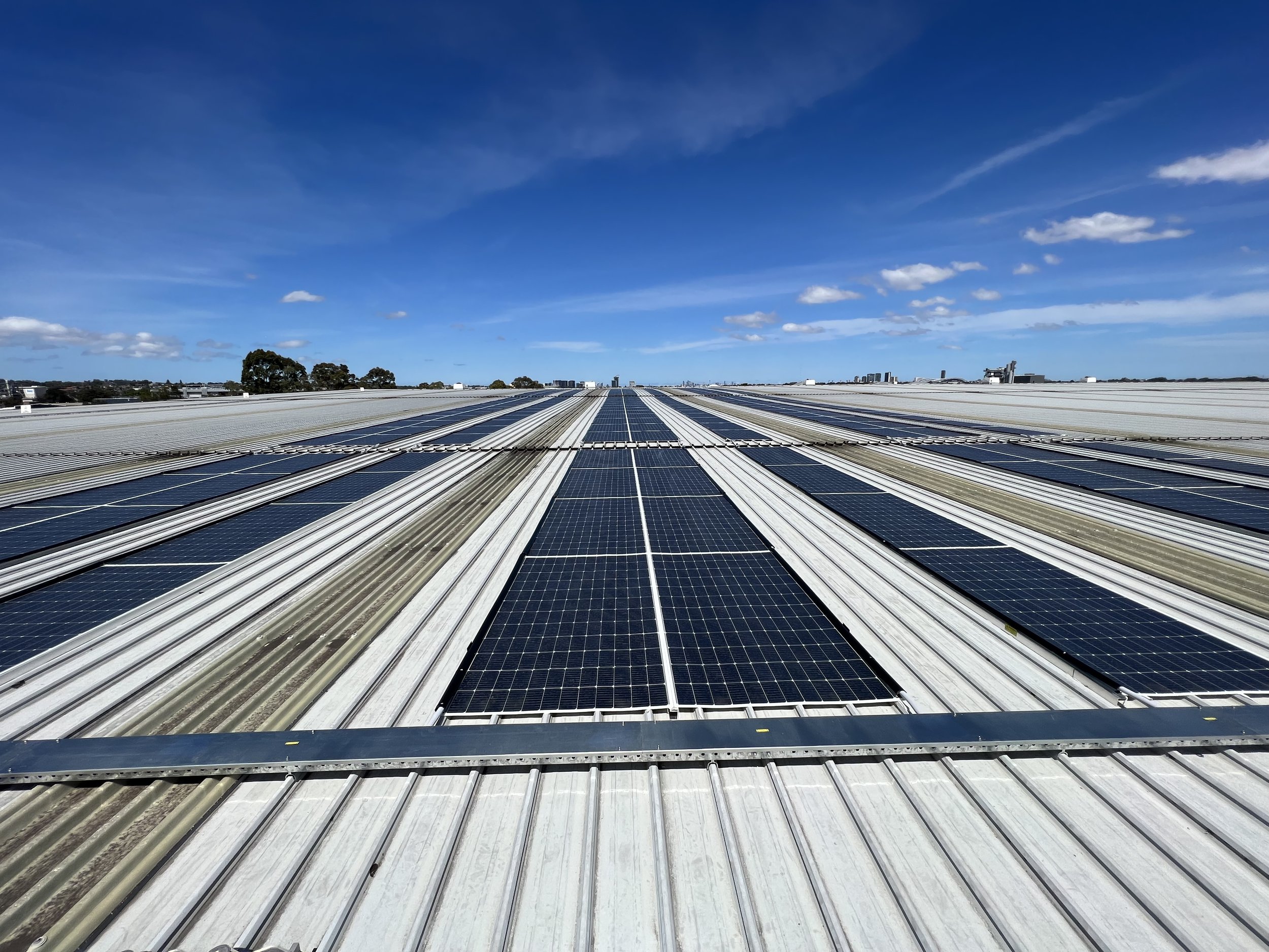 Rooftop solar panels under a blue sky with scattered clouds.