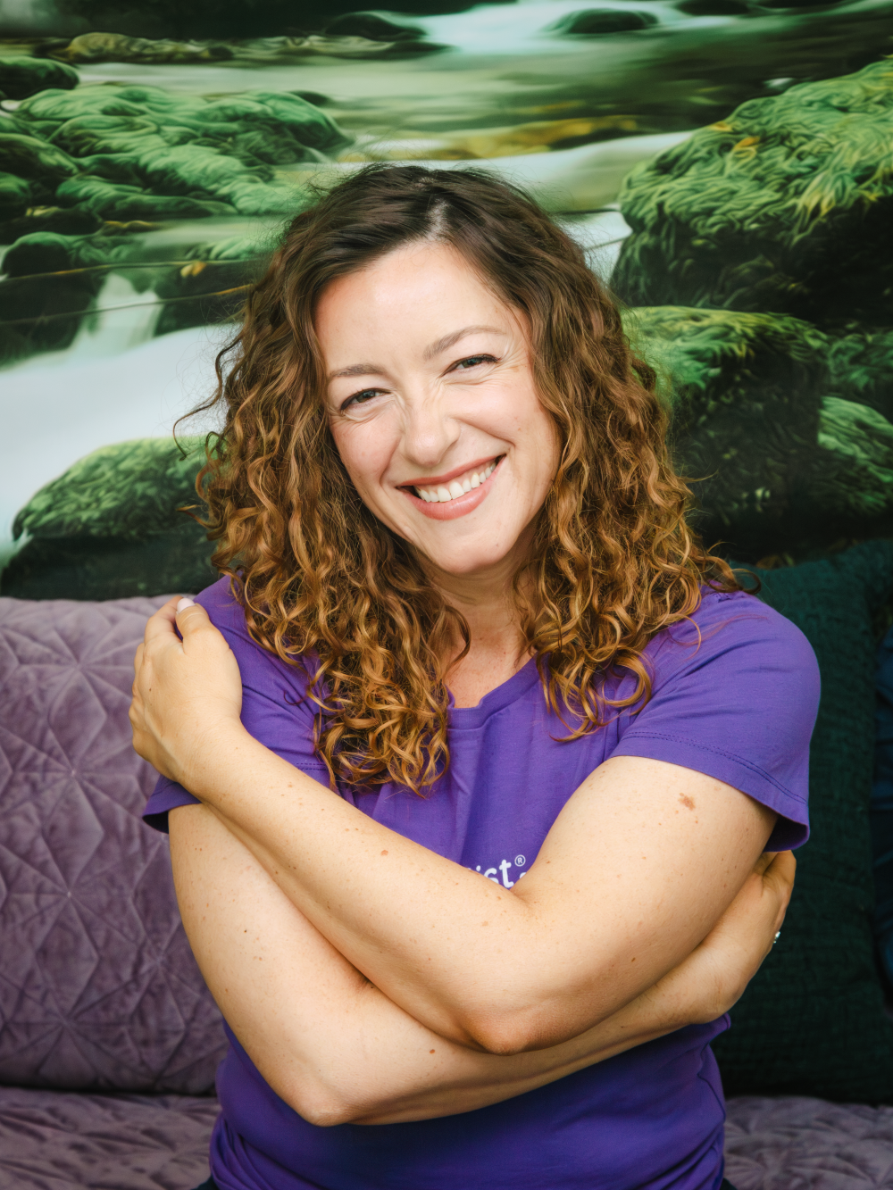 Ilona wearing a purple Cuddlist shirt, smiling broadly at the camera while giving herself a hug.