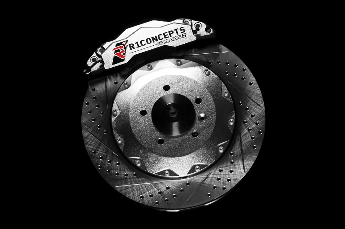 A high-performance car brake system featuring a R1 Concepts Forged Series 6 brake caliper and a slotted, ventilated brake disc.