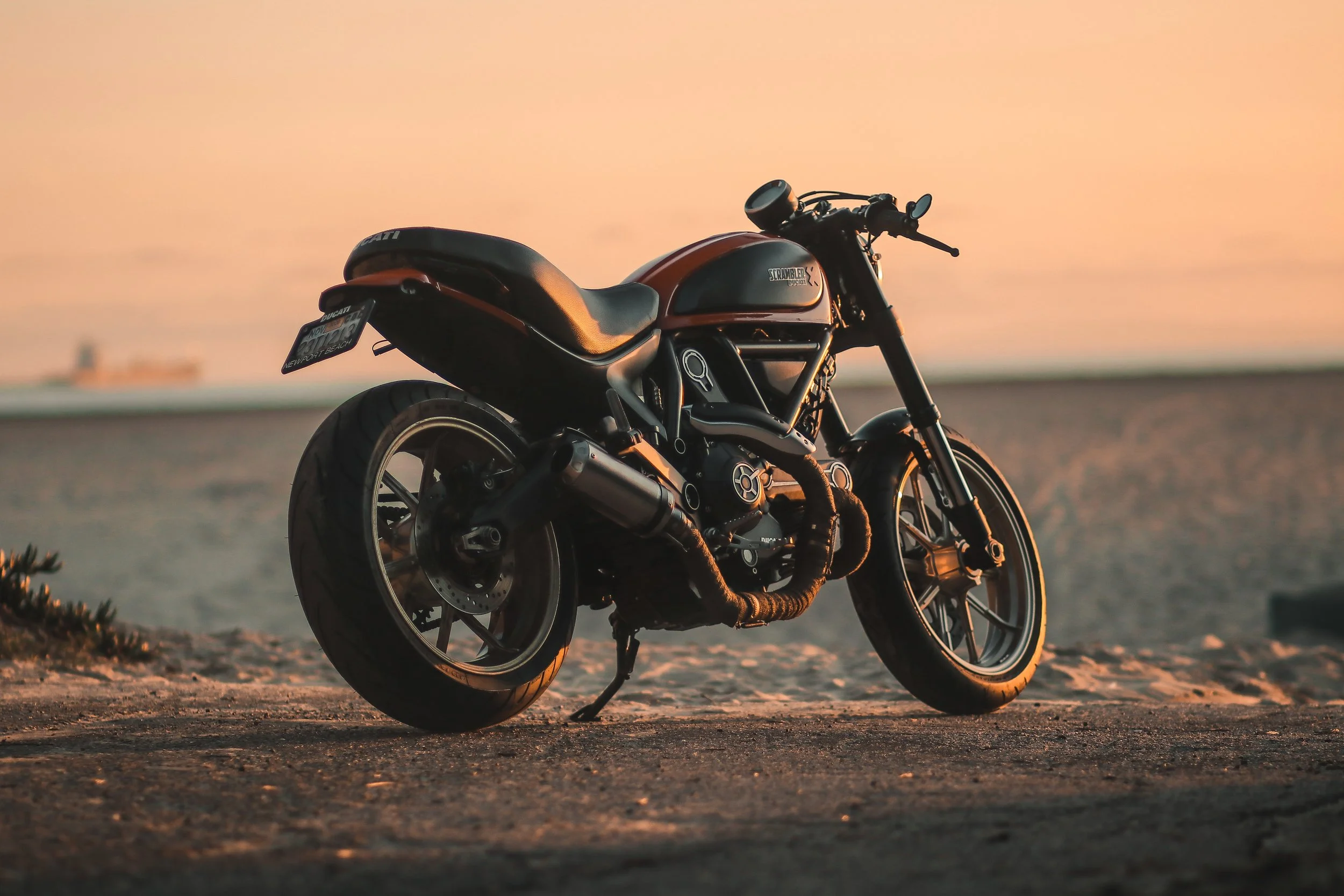 A black and orange Harley-Davidson motorcycle parked on a sandy surface at sunset.
