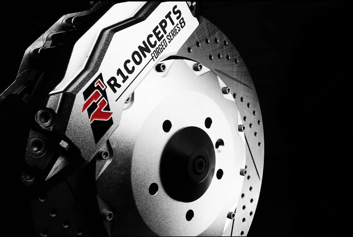 Close-up of a high-performance brake disc and caliper, with branding that says "R1 Concepts" and "Forged Series 8".