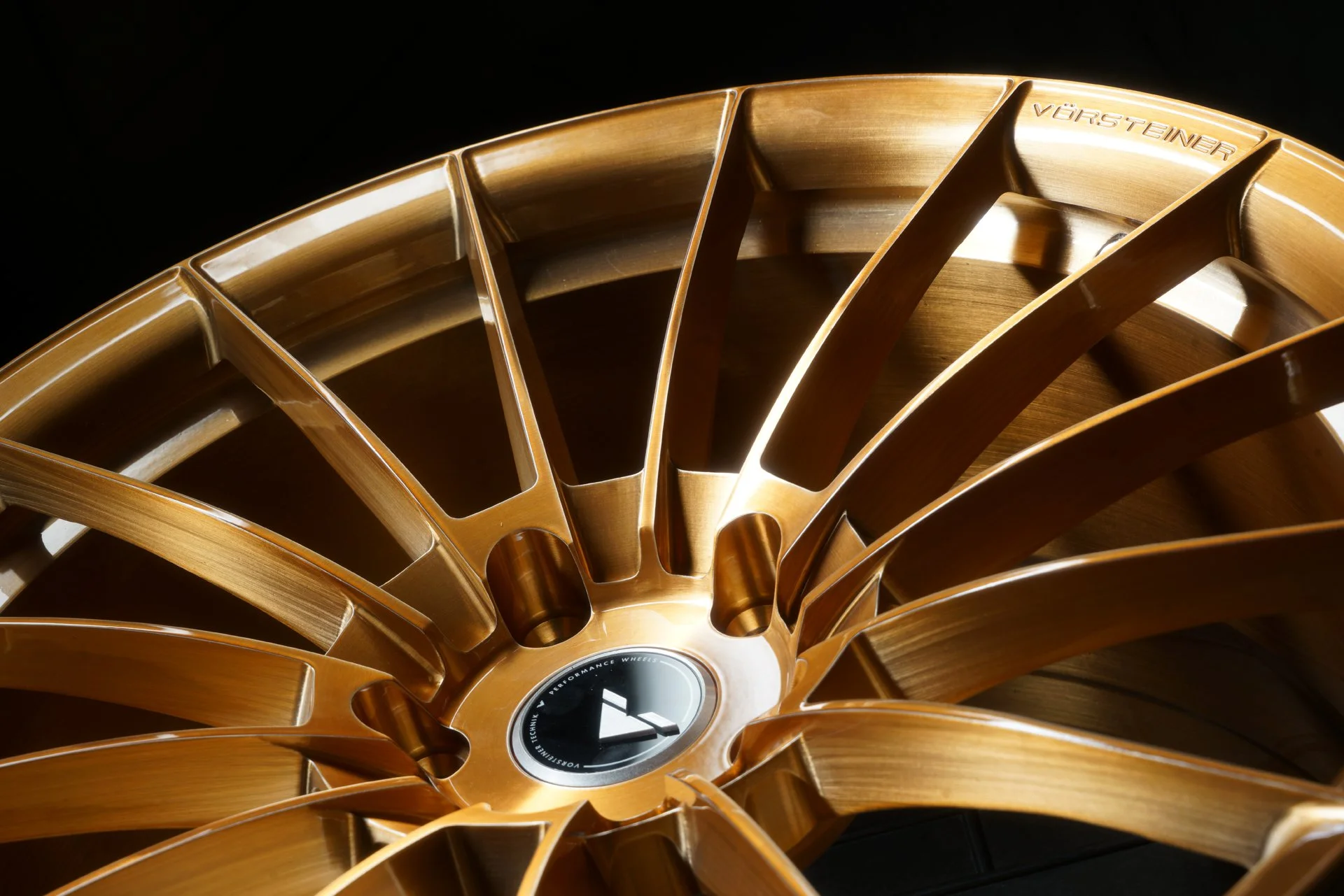 Close-up of a gold-colored alloy wheel with a spoke design, set against a black background.