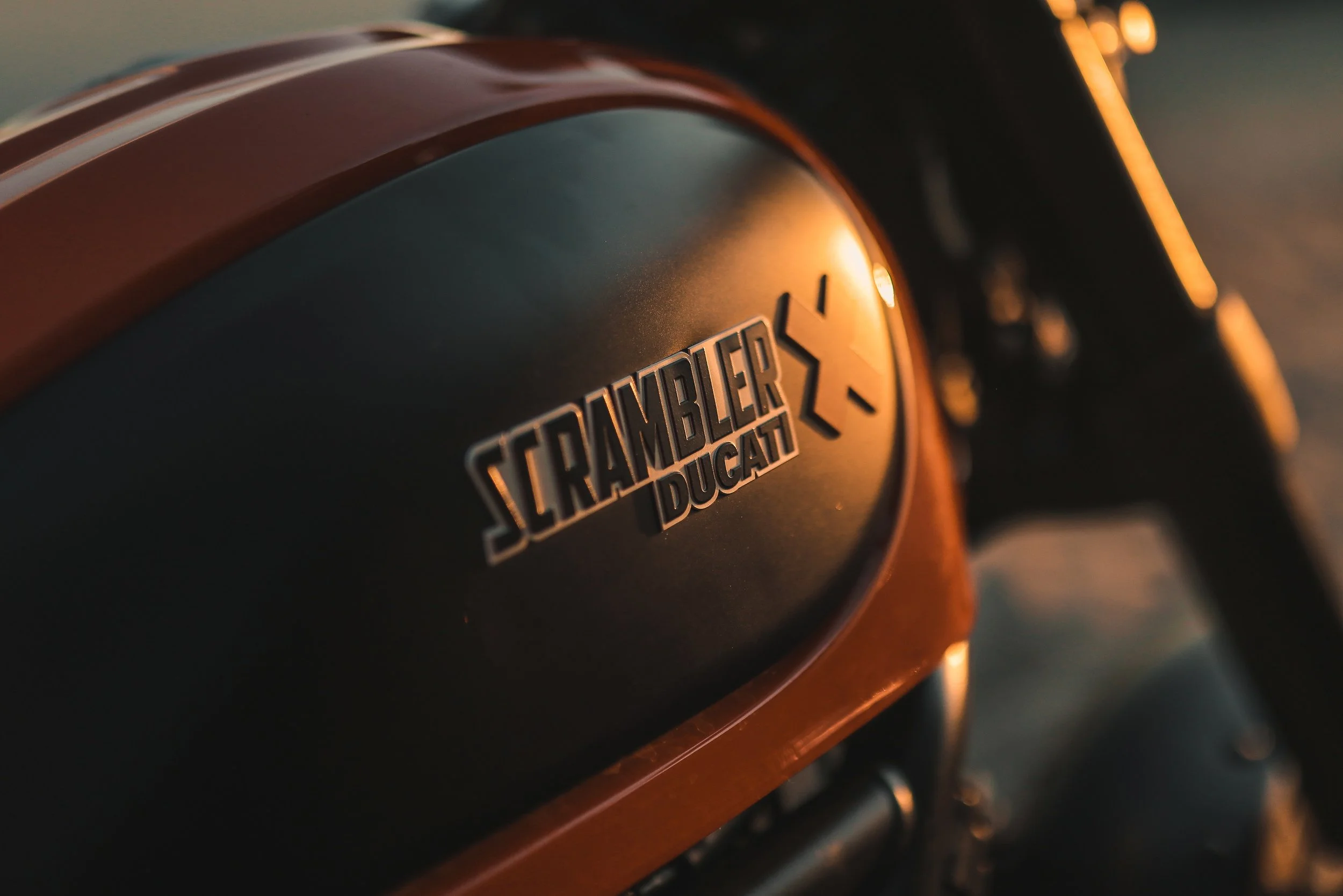 Close-up of a Ducati Scrambler motorcycle tank with the Scrambler Ducati logo.