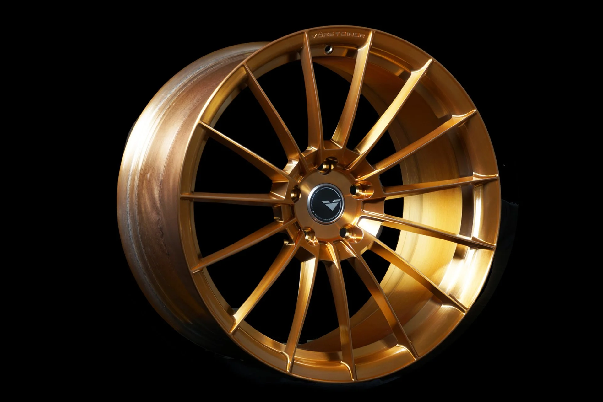 A gold-colored, multi-spoke alloy wheel with a black center cap, set against a black background.