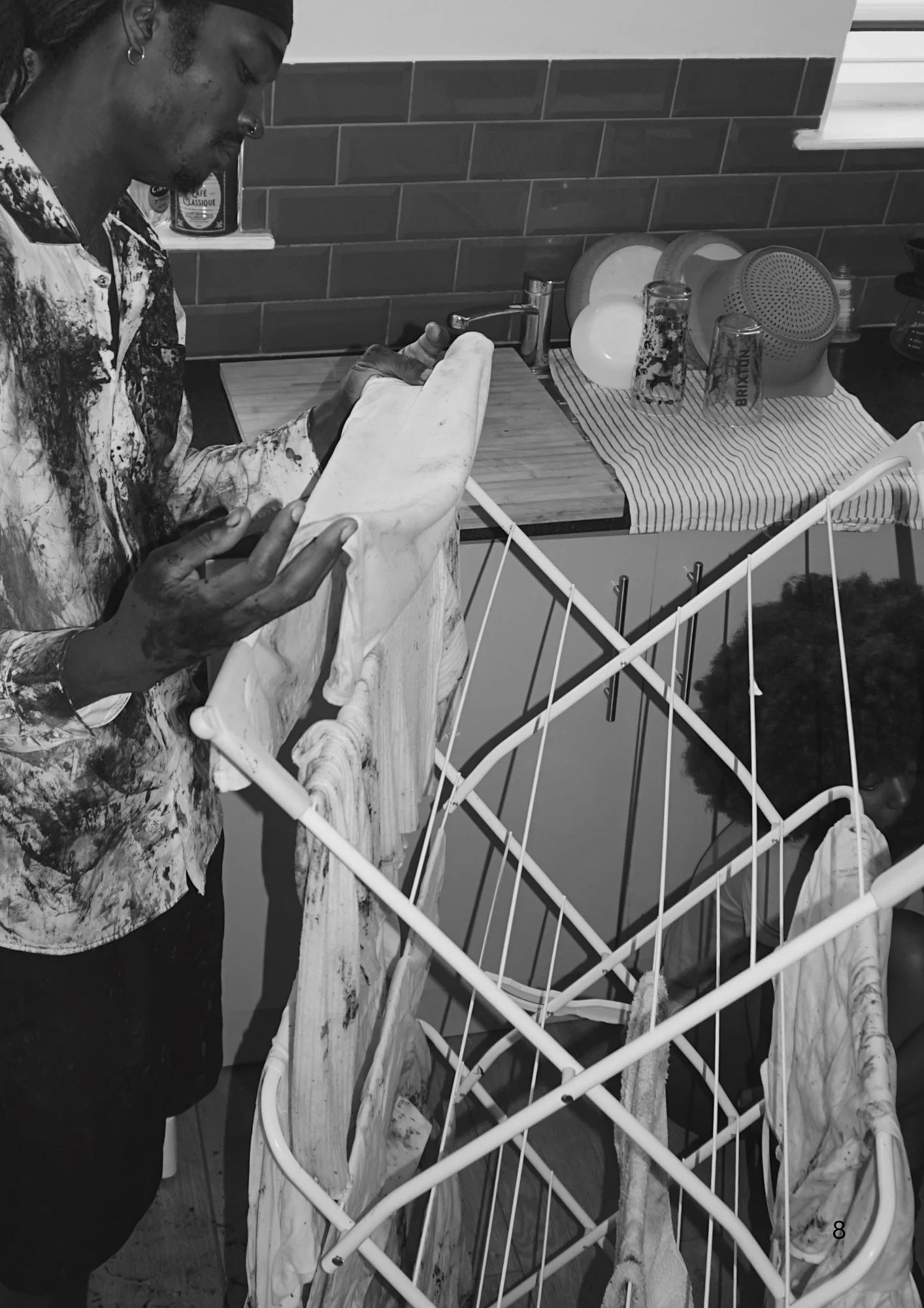 A person standing in a kitchen, drying a towel over a drying rack with plates, glasses, and kitchenware nearby.