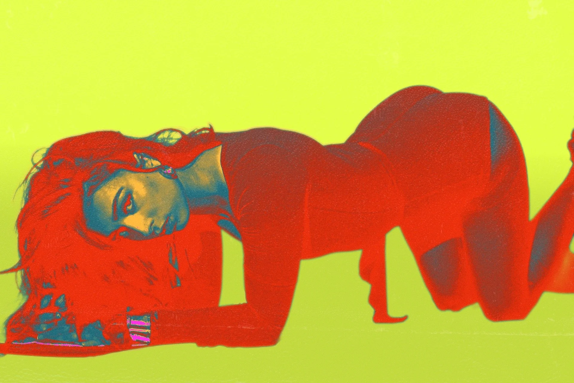 A woman with red hair lying on her side on a bright lime green background, with her head resting on her arm and looking at the camera.