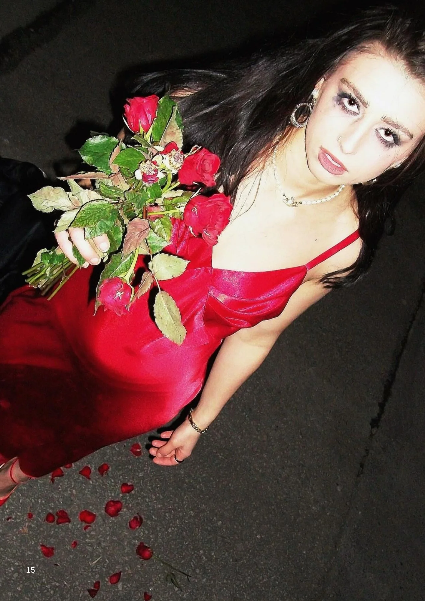A woman in a red dress holding a rose bouquet, with rose petals scattered on the ground, seen from a high angle.