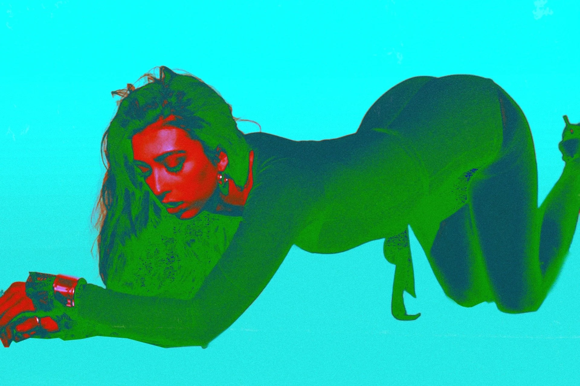 A woman with long hair lying on her stomach, propped up on her elbows, wearing a black outfit, with a bright blue background.