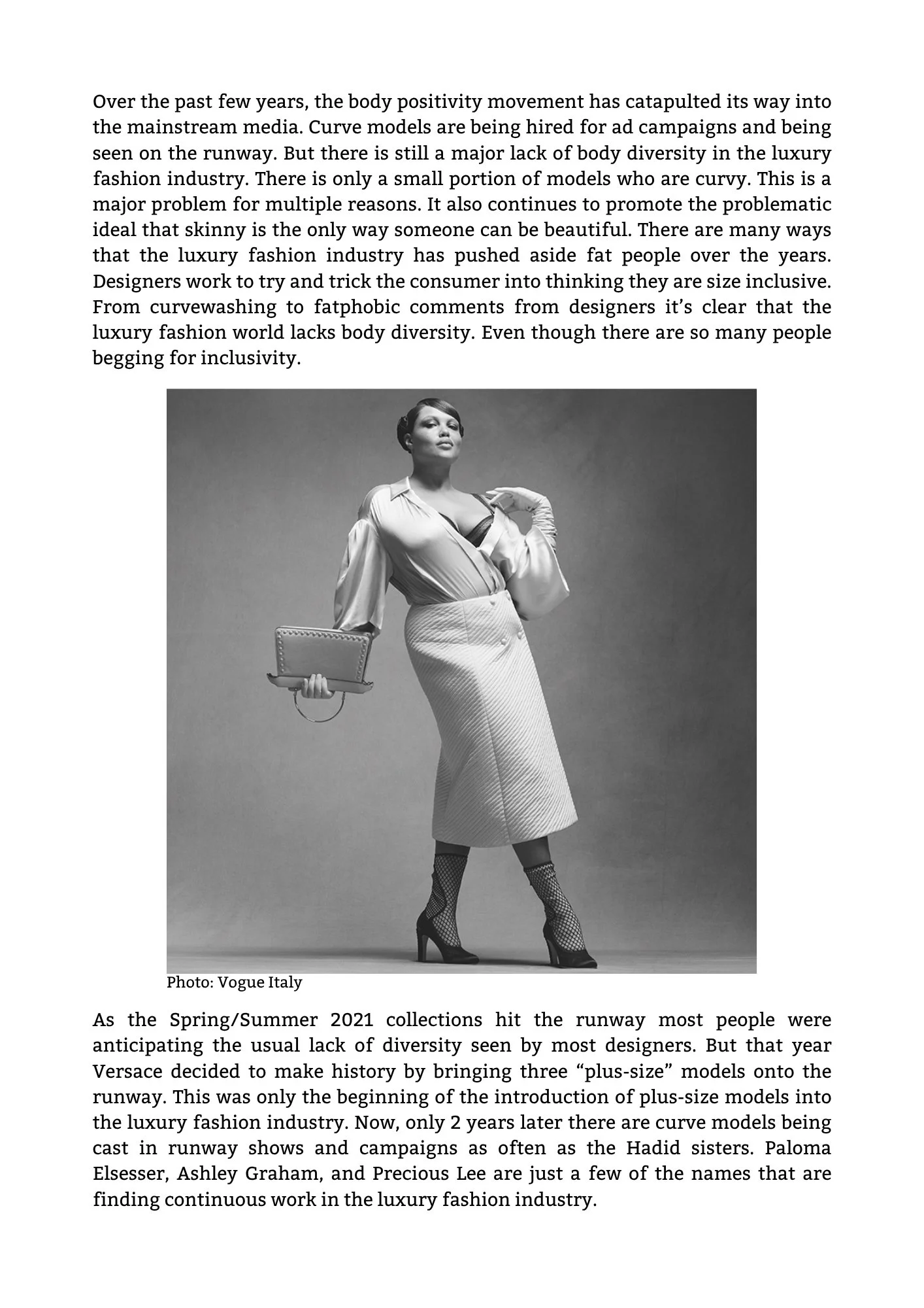 A black-and-white photograph of a plus-size female model in high heels, a blouse, and a long skirt, posing confidently with one hand on her chest and holding a clutch in the other.