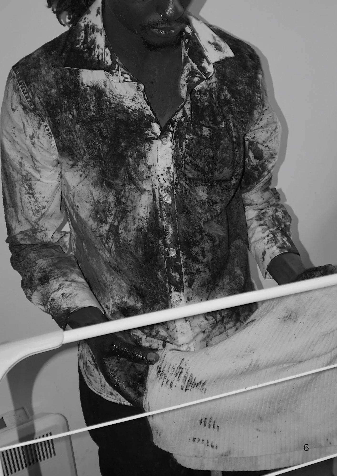 A person wearing a patterned, button-up shirt sitting at a table, partially visible through a white railing, with some equipment or appliances in the background.