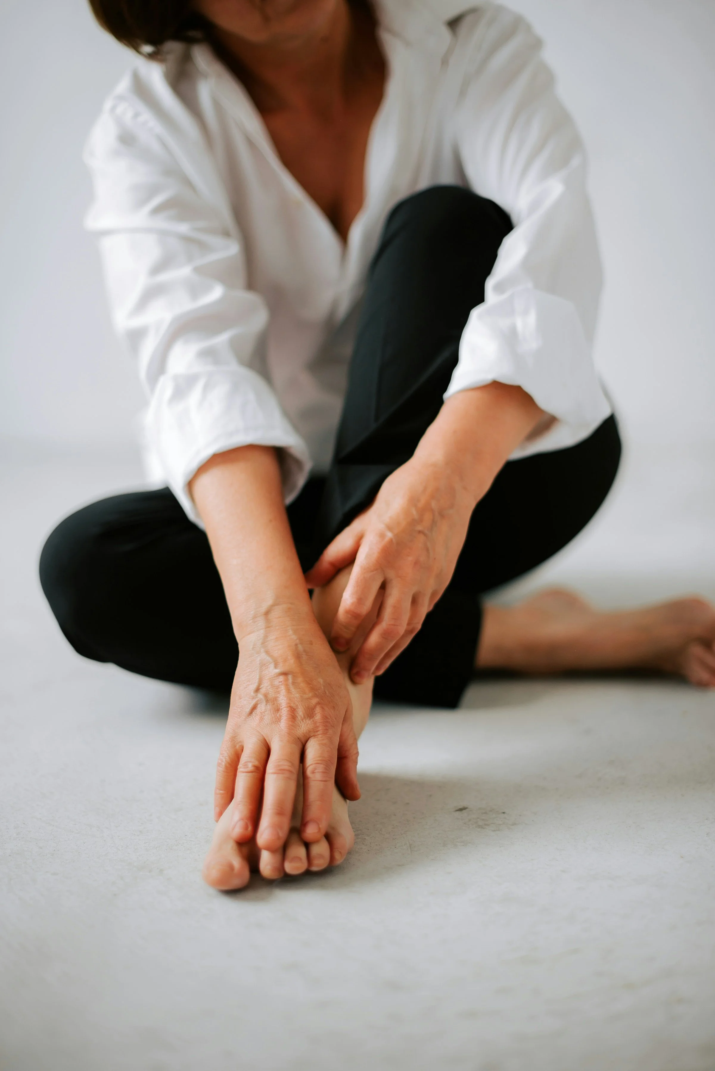 Calm woman sitting cross-legged on the floor with hands on feet, reflecting on chronic pain management strategies.