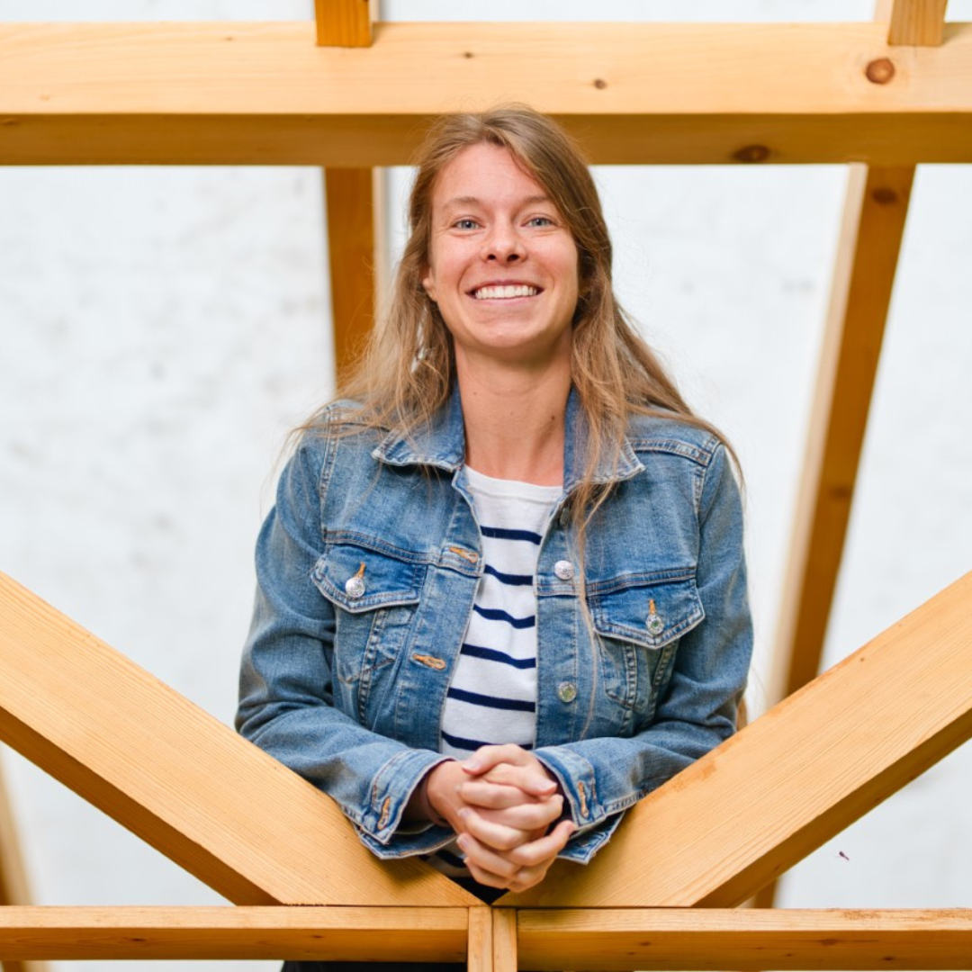 Person smiling in a denim jacket with wooden beams in the background.