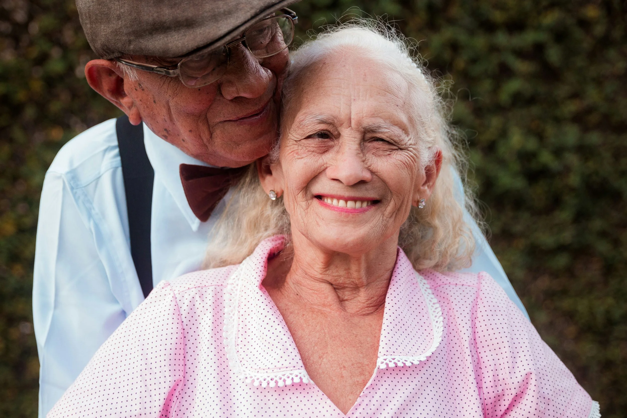 Smiling older lady being hugged by husband wearing hat and glasses