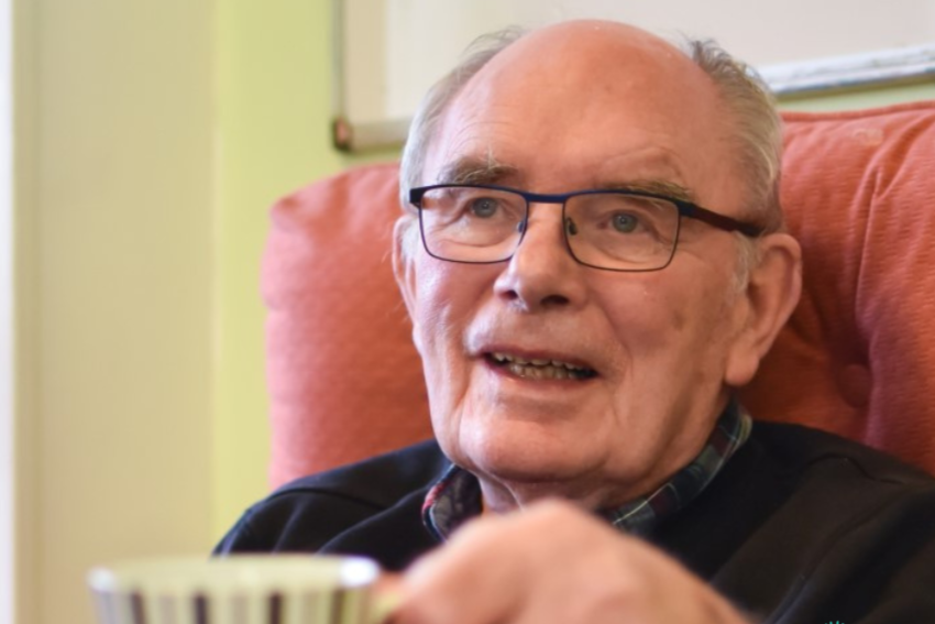 Smiling gentleman wearing glasses and holding up a mug of tea.