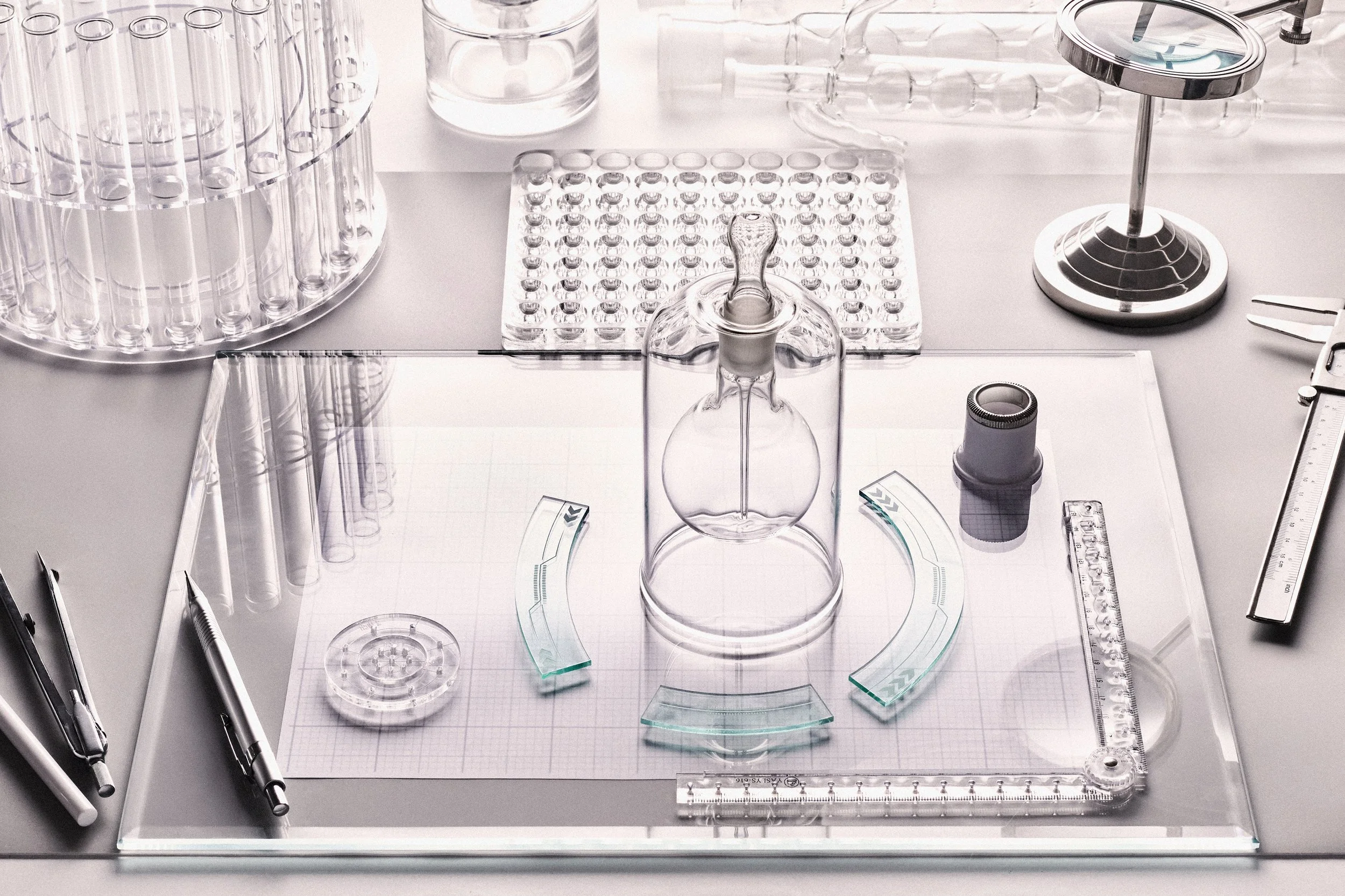 Laboratory setup with glassware, test tubes, a glass flask, rulers, pens, and lab instruments on a white work surface.