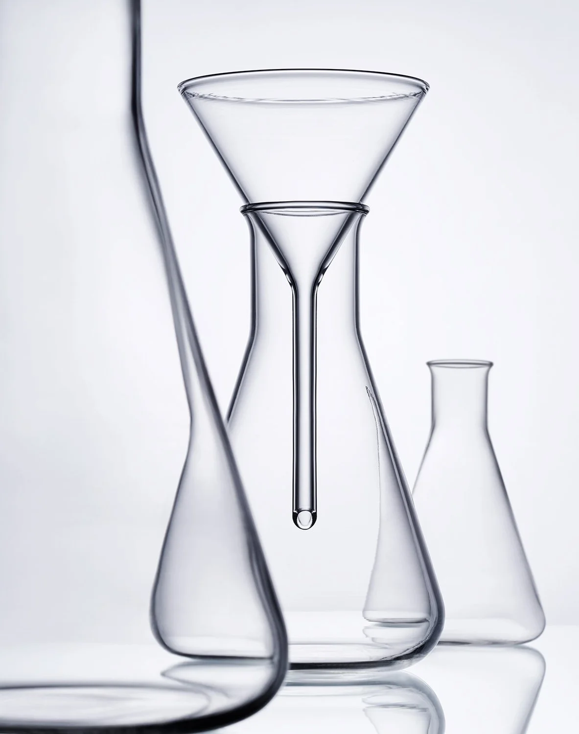 Multiple glass laboratory flasks and a dropper with a droplet of liquid, set against a white background.