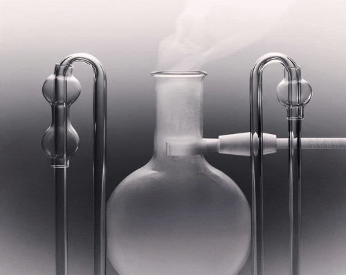 A laboratory distillation apparatus with glassware and metal supports, emitting vapor or steam from the top of the flask.