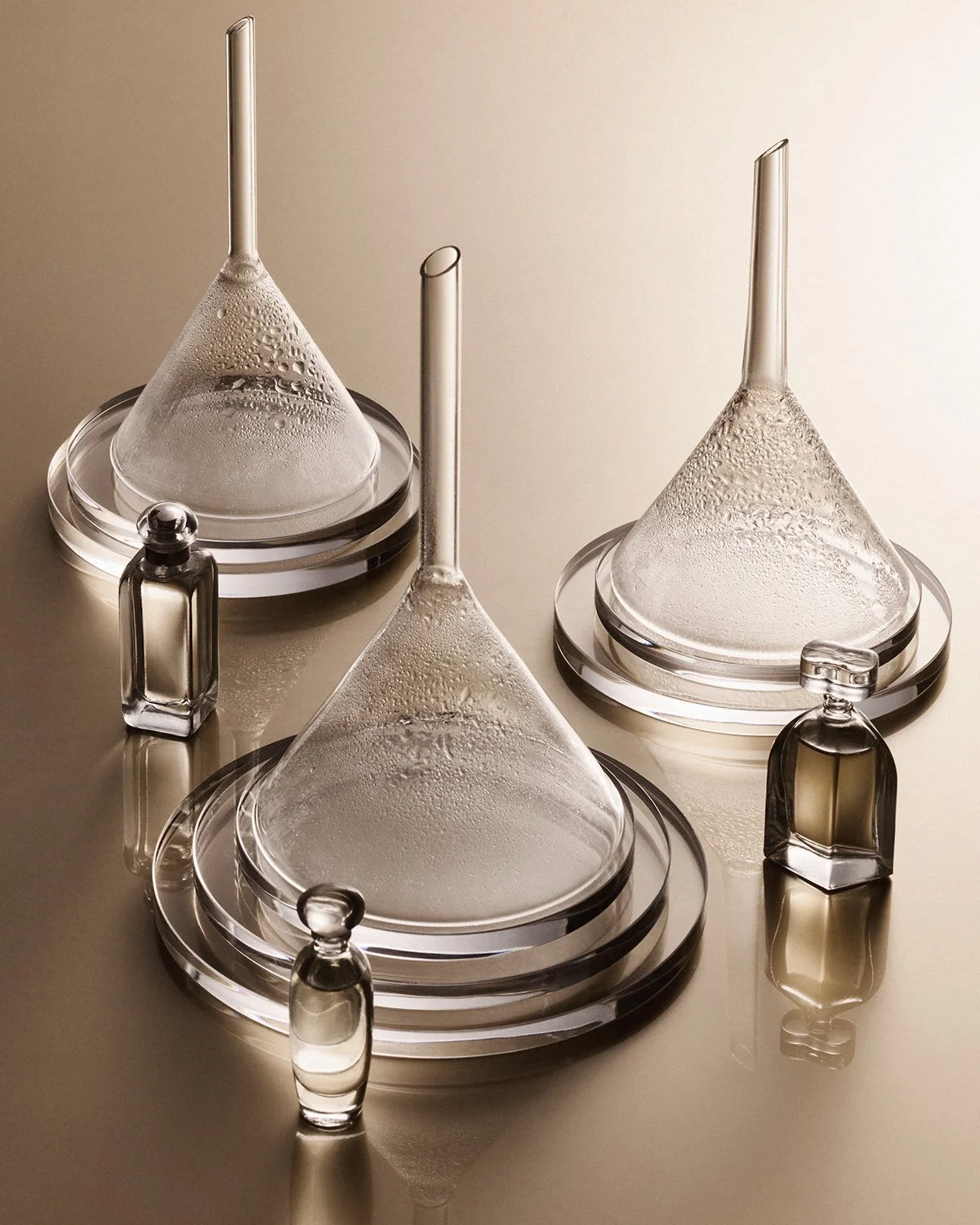 Three Petri dishes with conical shapes and three small glass bottles on a reflective surface.