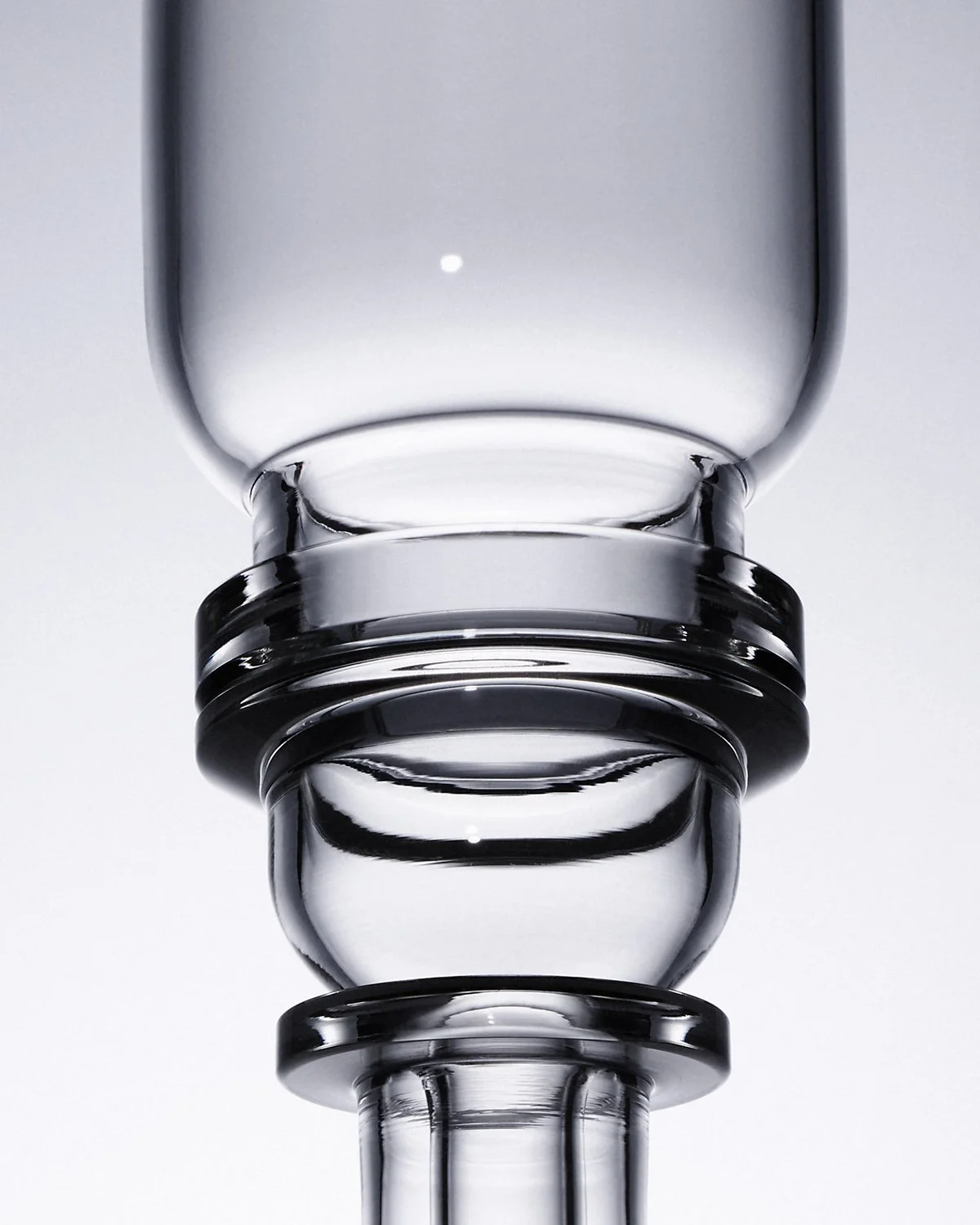 Close-up of a clear glass vase with a rounded bottom and a narrow neck, photographed from below with a white background.