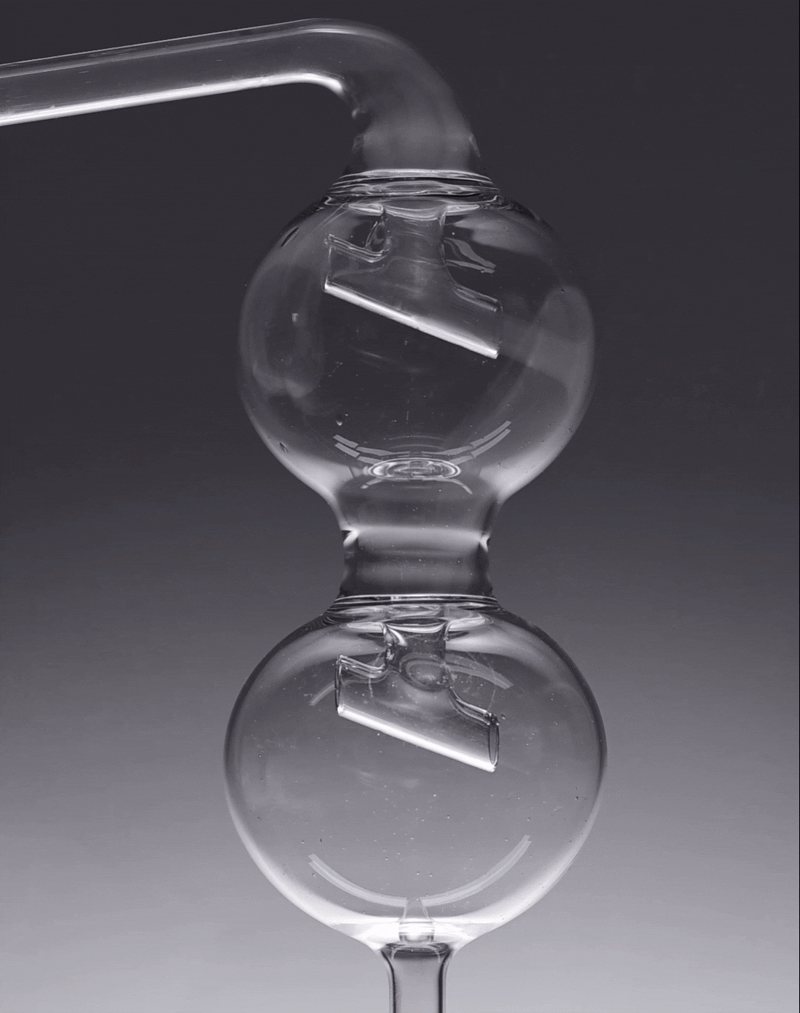 A glass sculpture with two interconnected spherical glass orbs, reflecting light, against a dark background.