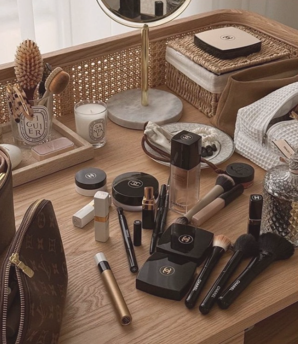 Coiffeuse avec produits de maquillage Chanel, pinceaux, mascara, poudre, rouge à lèvres, miroir, bougies, et accessoires de beauté.