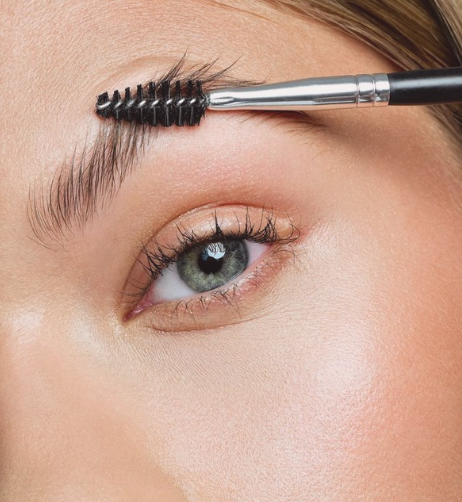 Un œil avec un pinceau de maquillage sur le sourcil.