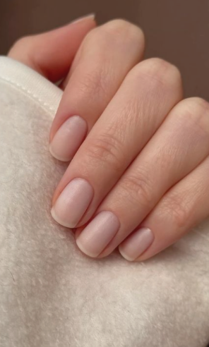 Main avec des ongles manucurés en couleurs naturelles, posée sur un tissu beige.