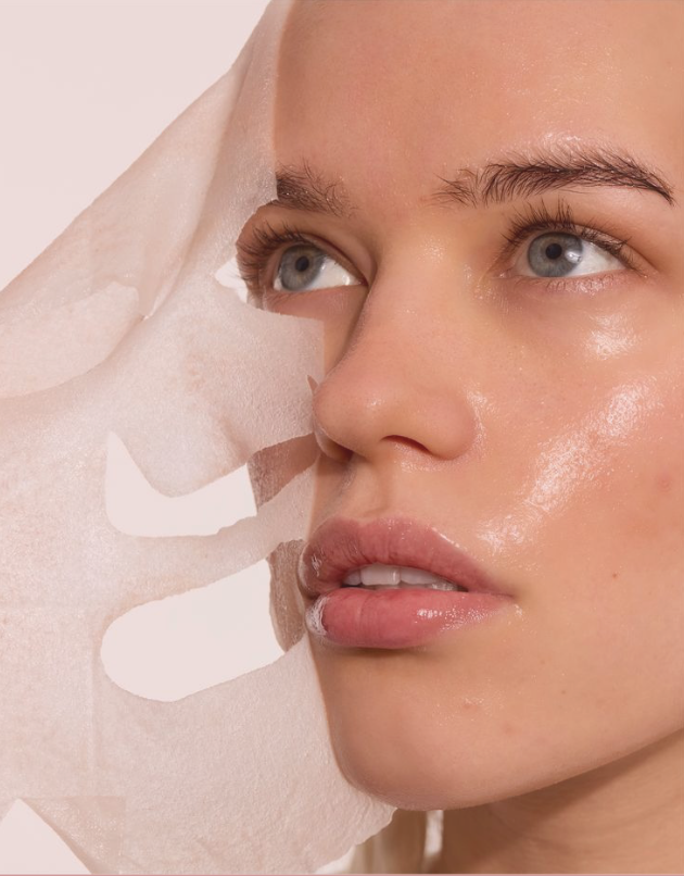 Une femme appliquant un masque facial en papier blanc sur son visage pour une routine de soin de la peau.