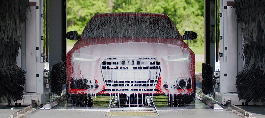 A red car being washed with water on an automatic car wash system.