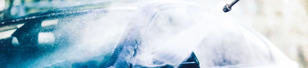 A car undergoing a high-pressure water cleaning, with water spray and steam visible.