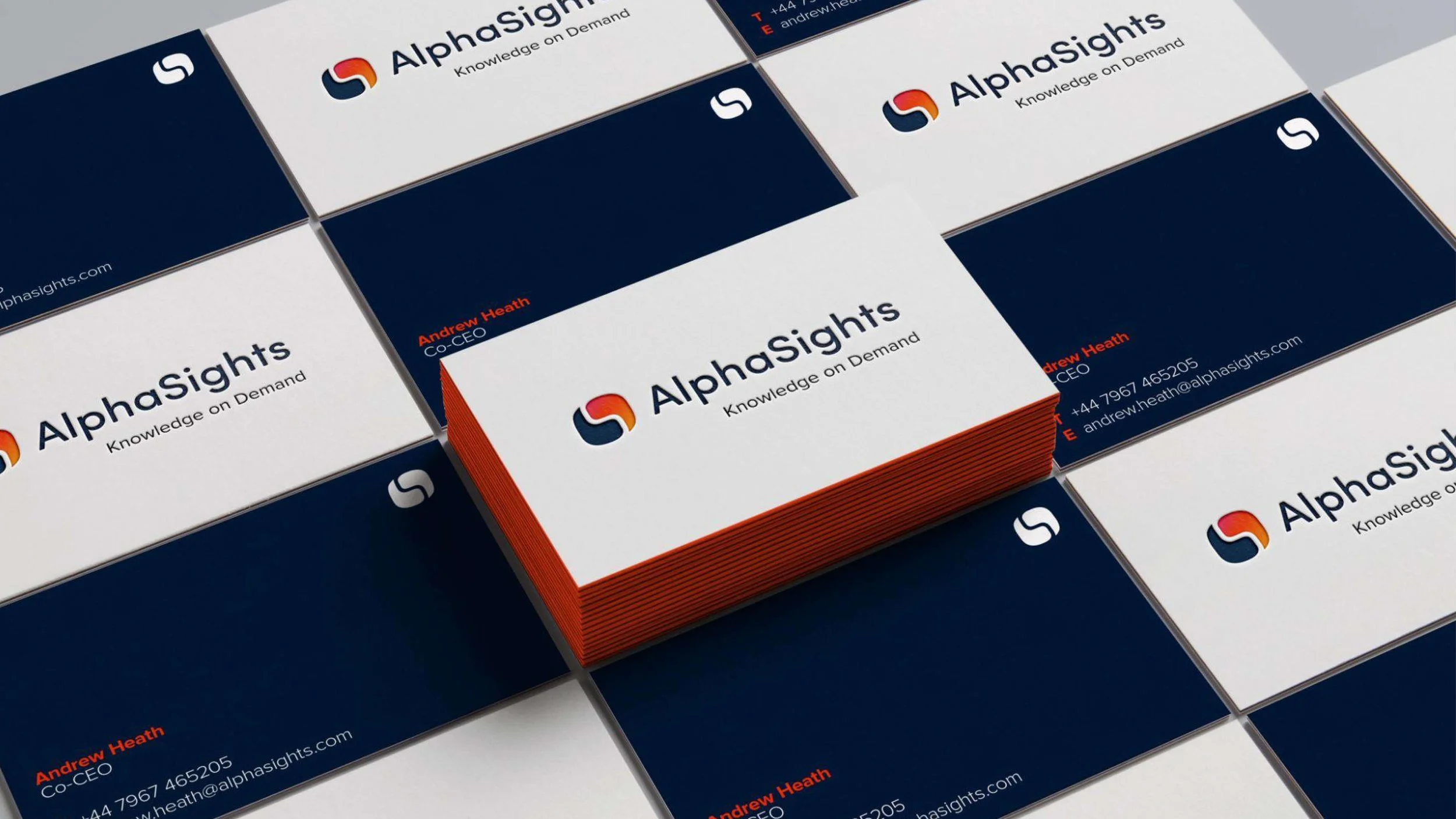 Multiple business cards for AlphaSights arranged in a grid pattern, with one stack prominently placed, displaying the company's logo, name, tagline 'Knowledge on Demand,' and contact details. The cards have a white background with the logo in red, navy blue, and orange, and text in navy blue and red.