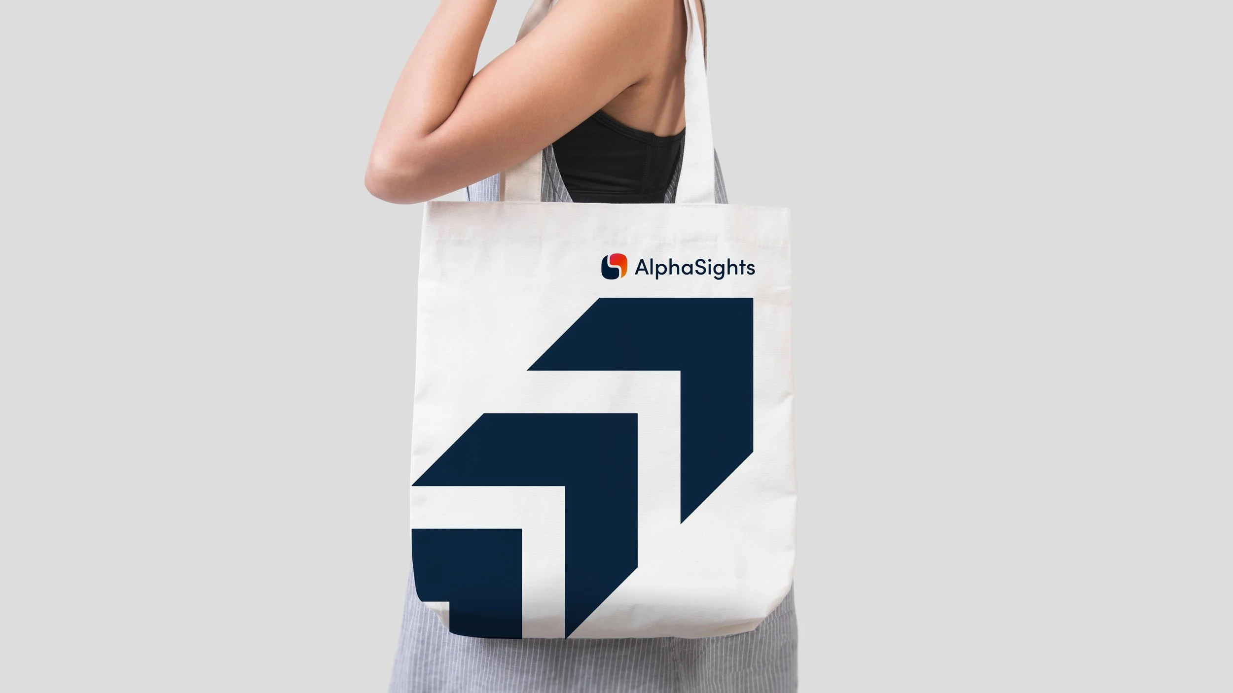 A person holding a white tote bag with a blue geometric design, the 'AlphaSights' logo, and the number '41' printed on it.