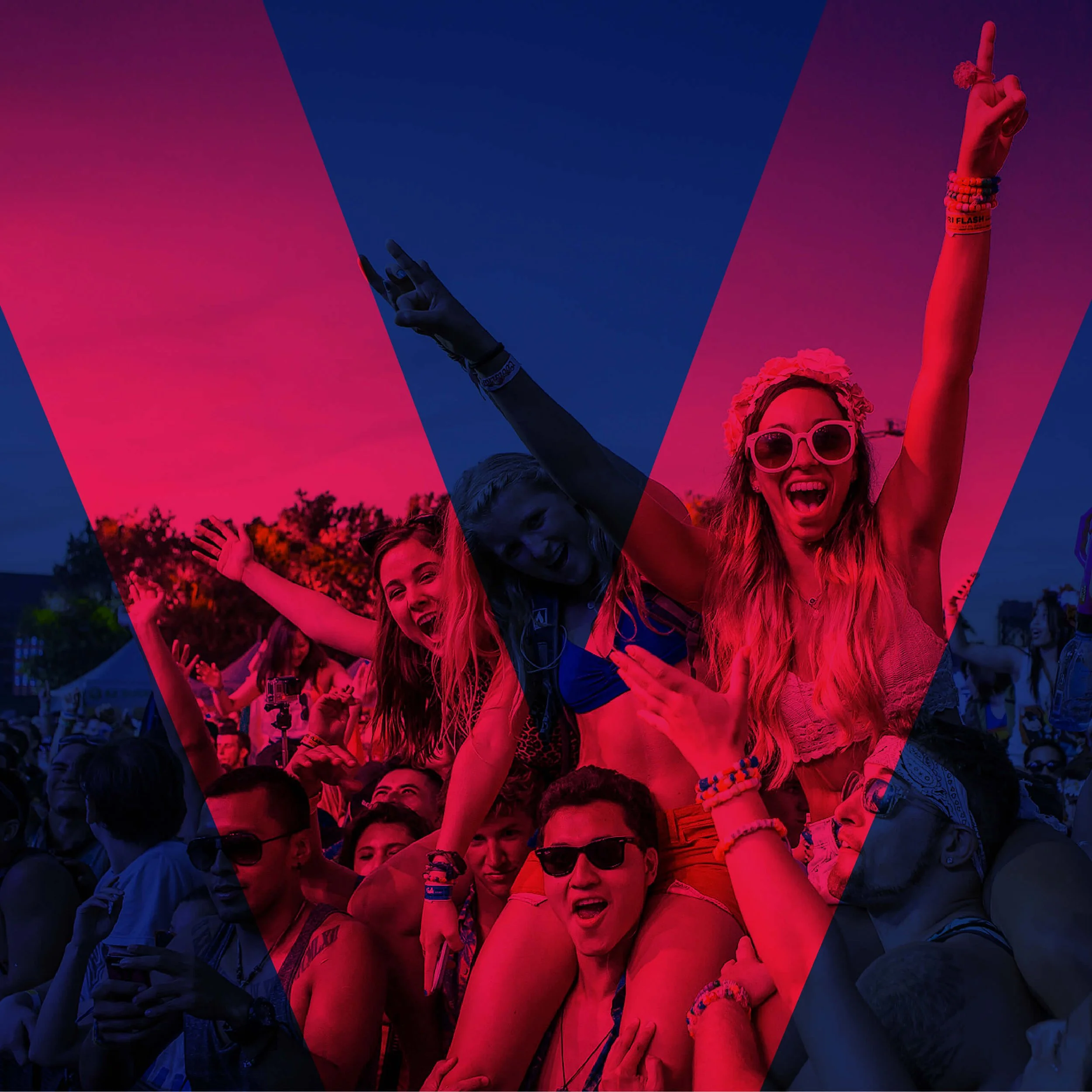 Group of people at a festival enjoying music, with a woman in sunglasses and a flower headband raising her hand and smiling.