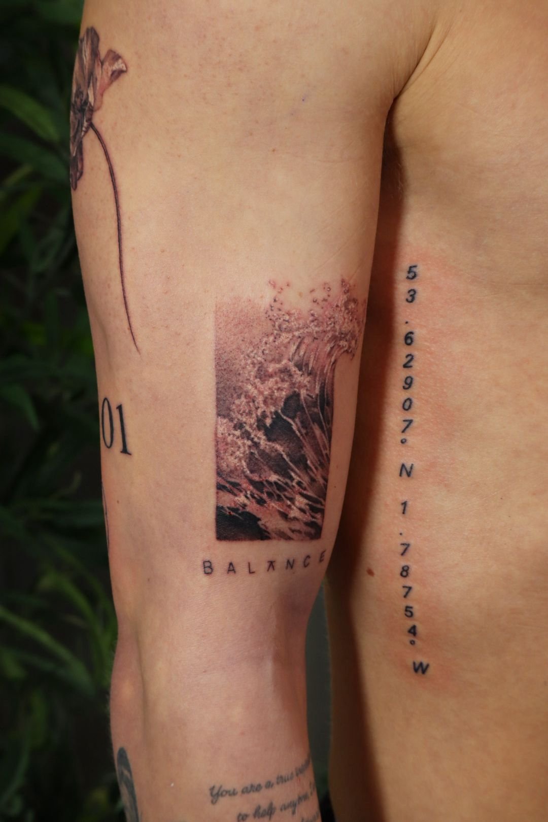 Person's arm with multiple tattoos, including floral design, the word 'BALANCE,' and coordinates.