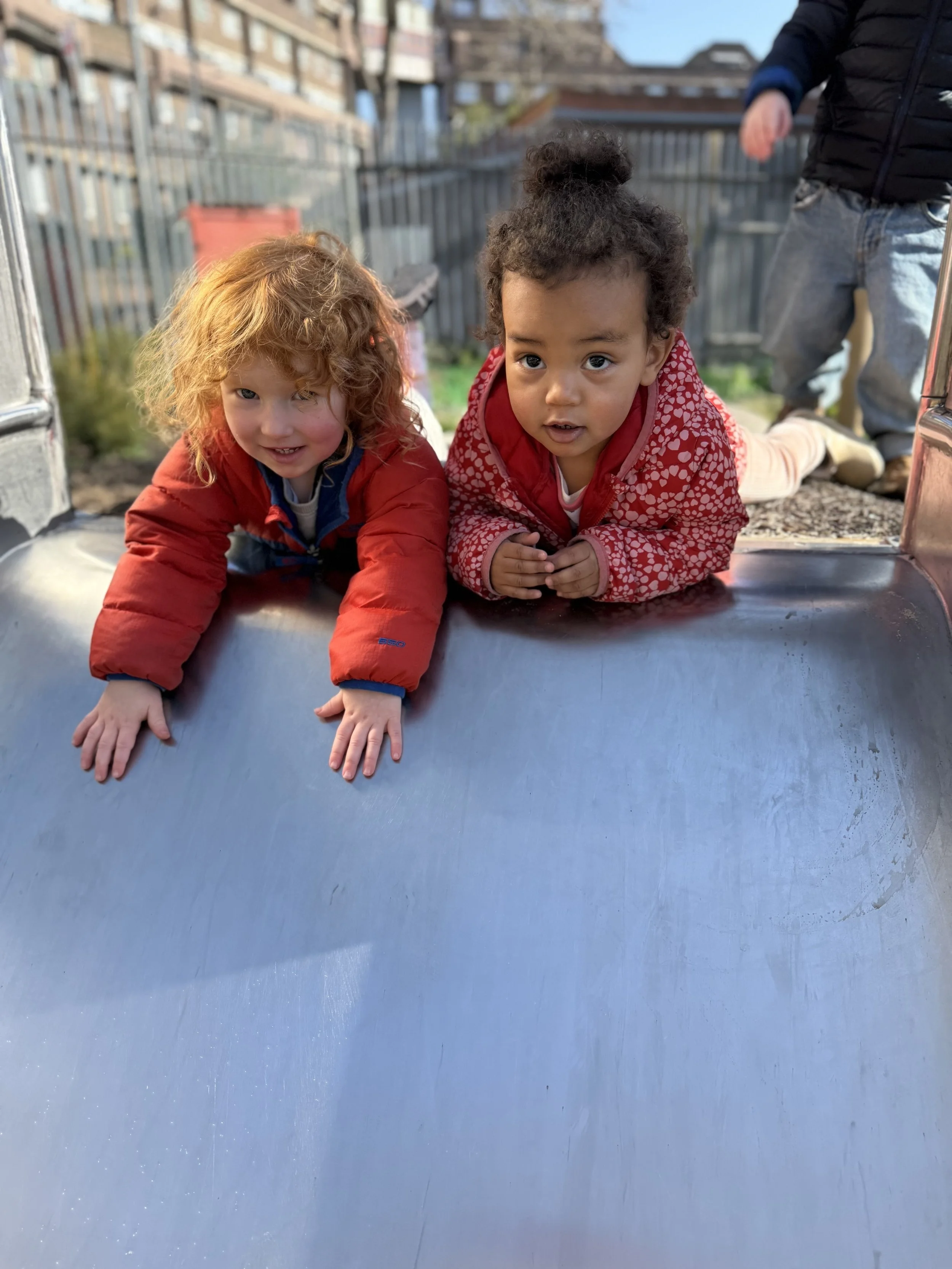Child sitting on grass, wearing a yellow sweatshirt and striped pants, looking through binoculars.