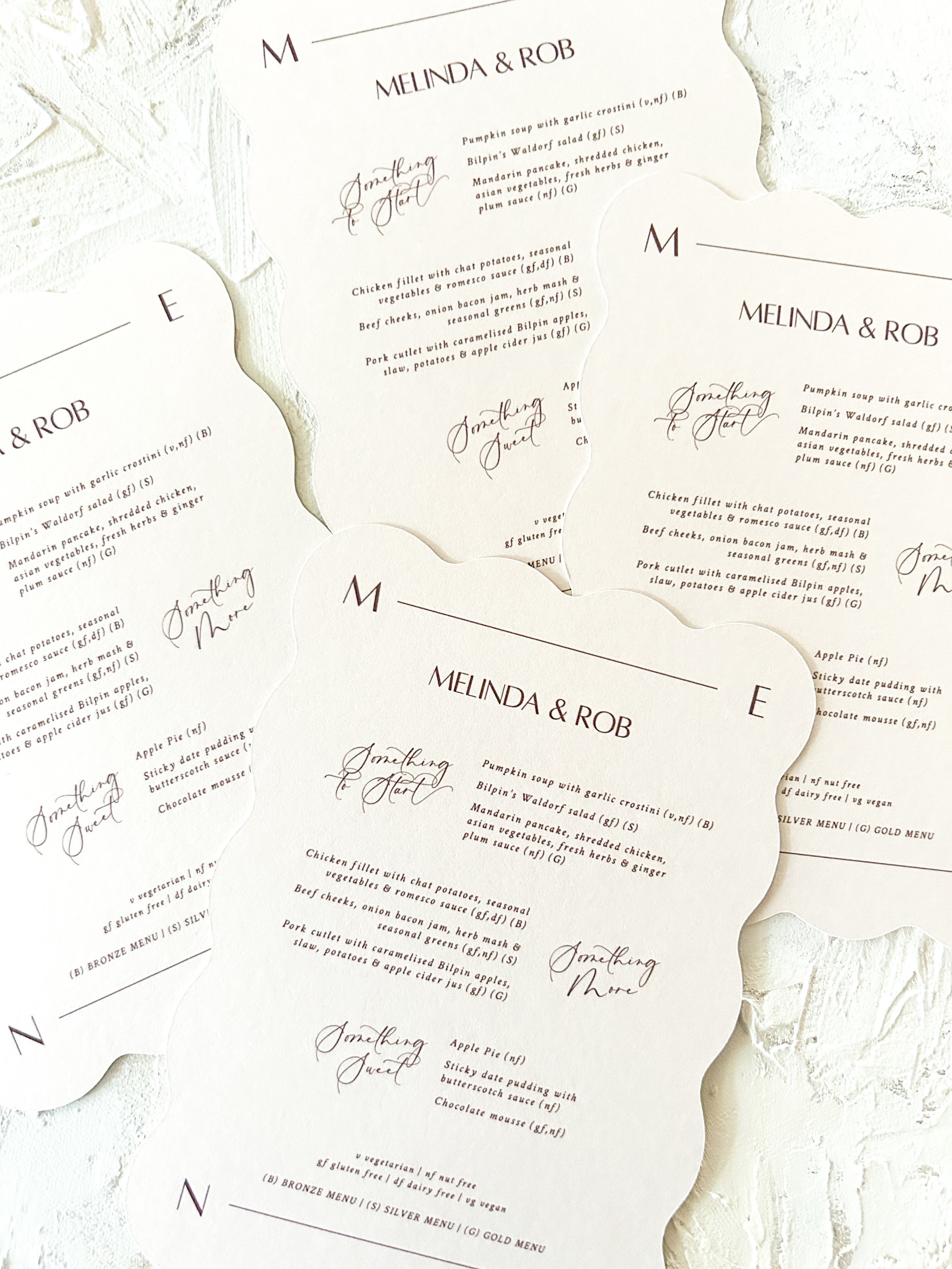 Wedding menu cards with a white textured background, featuring elegant black cursive and serif fonts, with some portions in all caps.