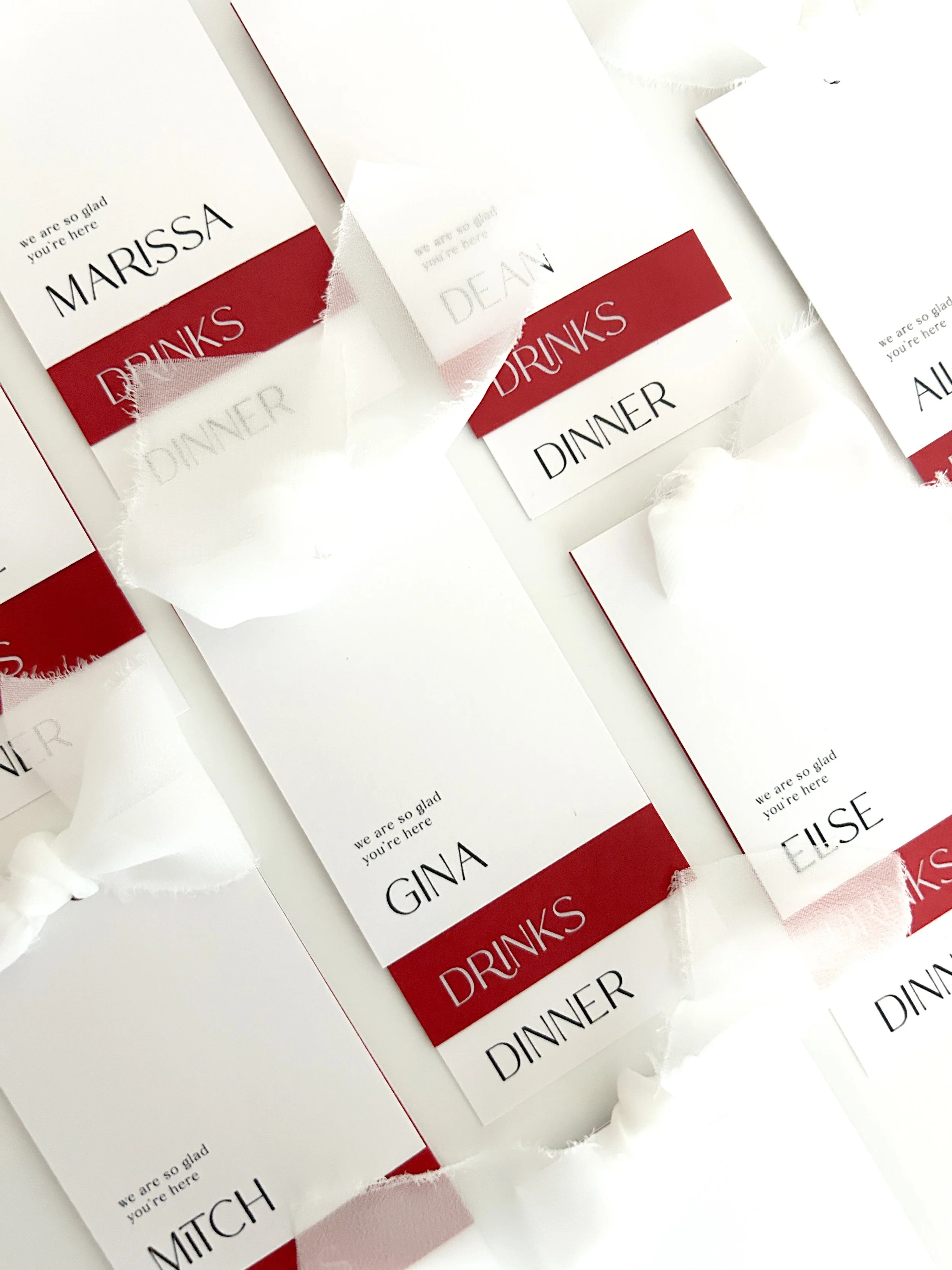 Table name tags for a dinner event with guest names 'MARIssa', 'GINA', 'ELISE', 'MITCH', and 'ALEX'. The tags are white with red and black text, and some are attached to torn white paper.